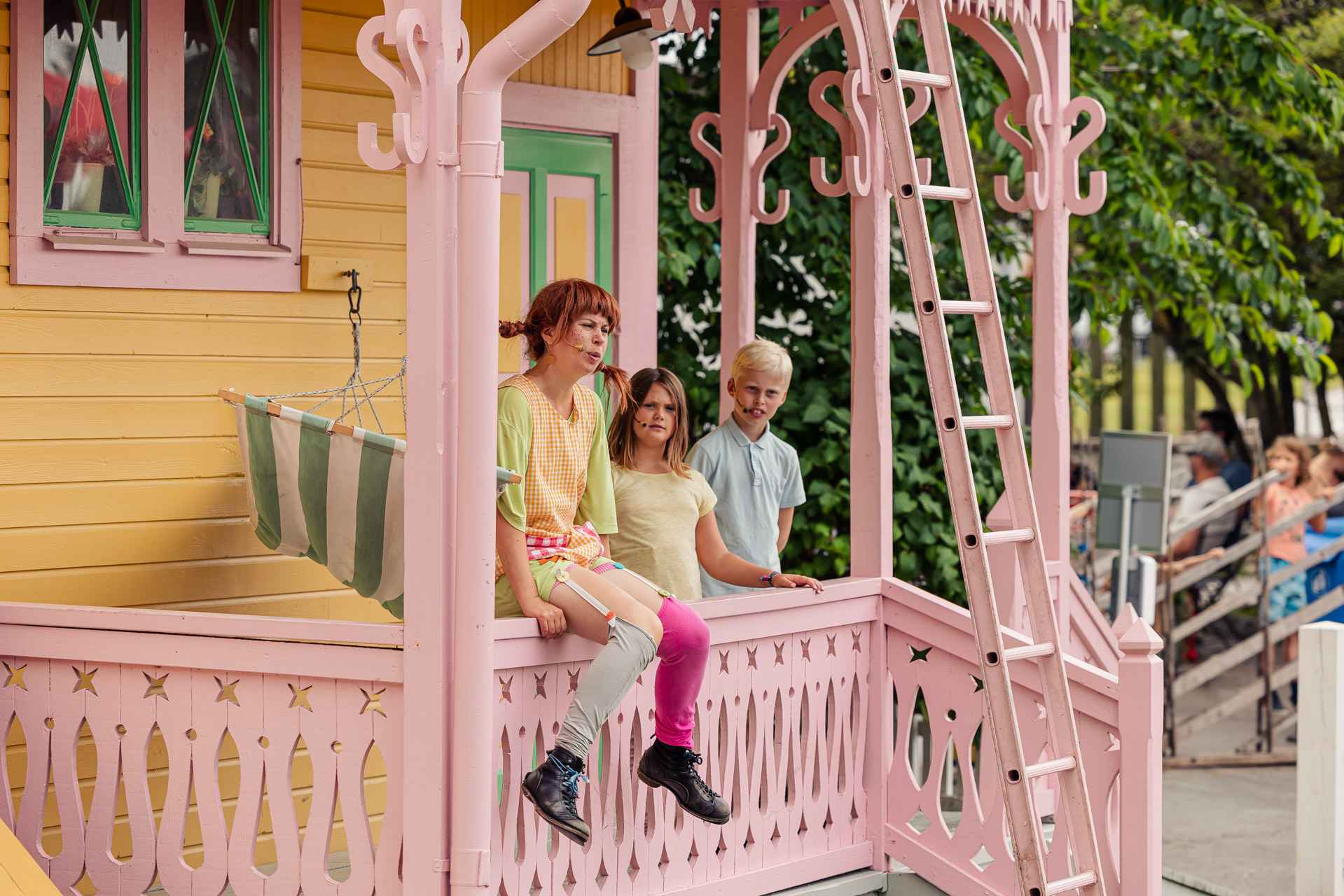 A theatre performance with Pippi Longstocking who is sitting on the porch at her yellow house, Tommy and Annika are standing by her side