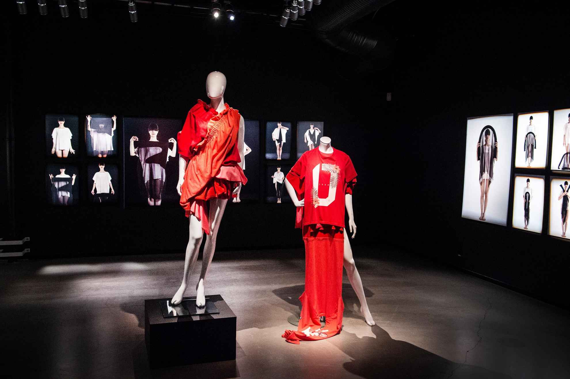 Mannequins dressed in red outfits, and large fashion photos hanging on the wall in a dark room.