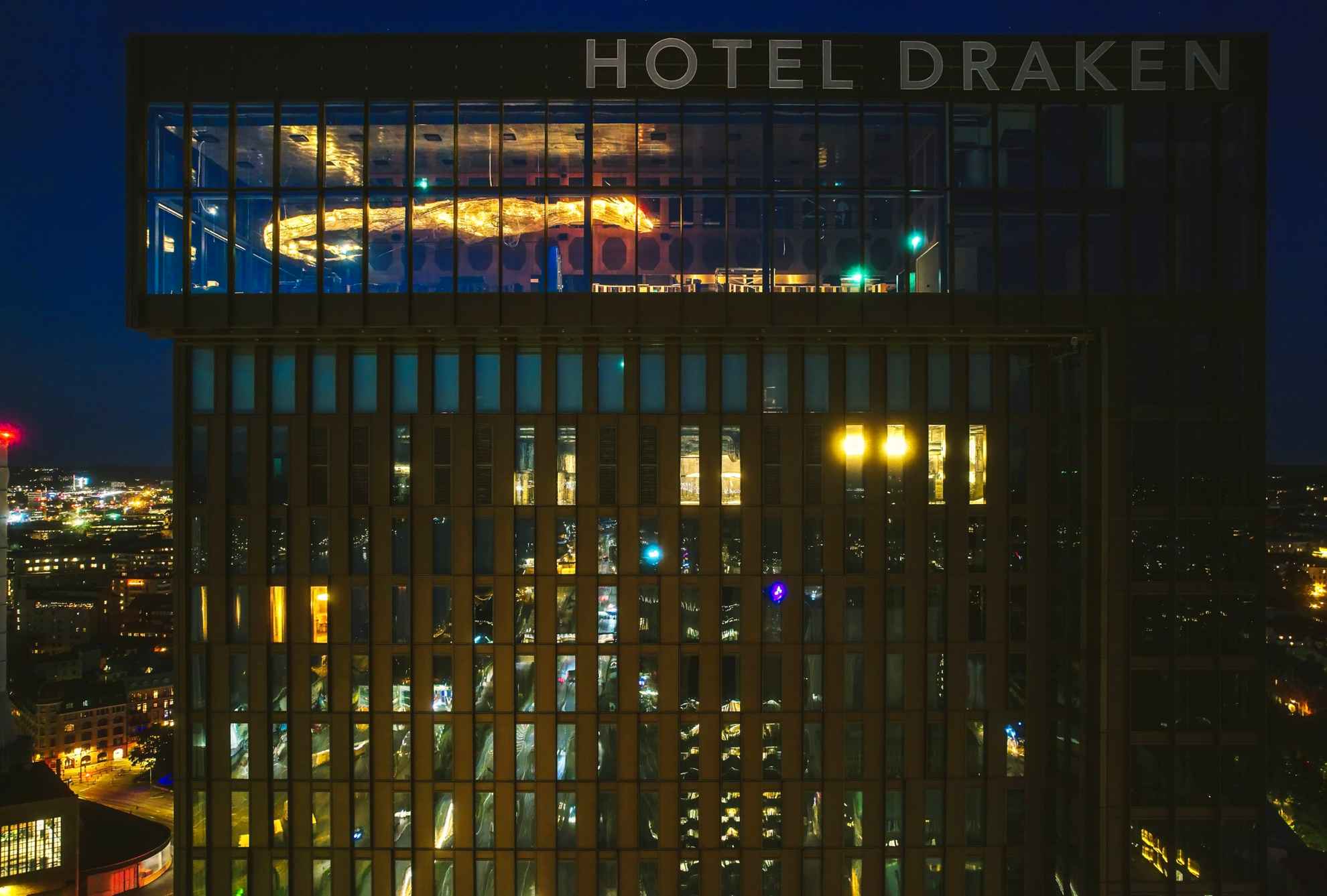 Clarion Hotel Draken at night, showcasing the illuminated exterior and the hotel's name displayed at the top of the building.