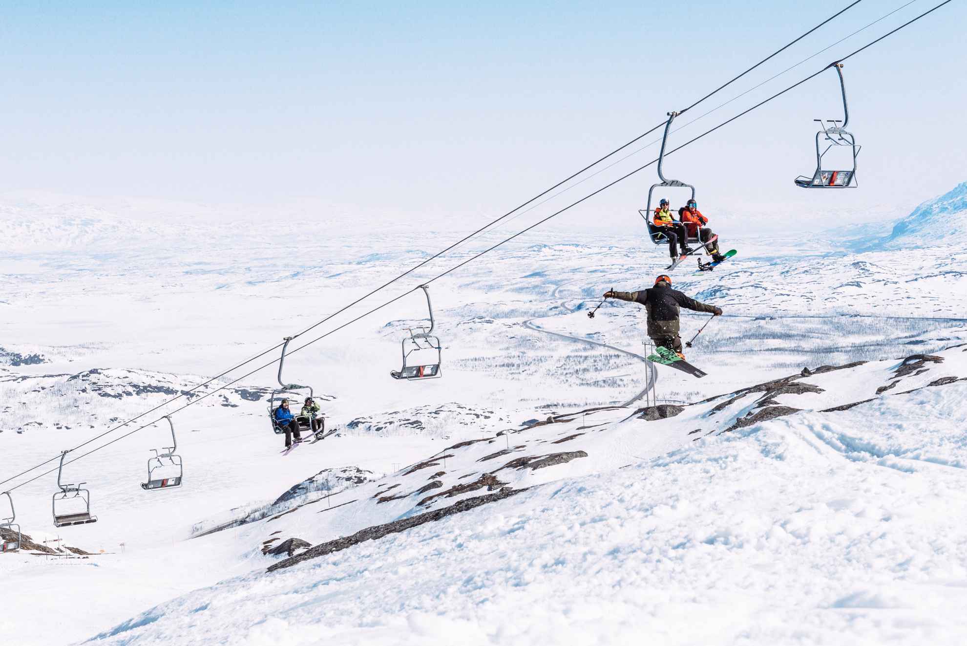 People sitting on a ski lift looking at a person jumping with skis.