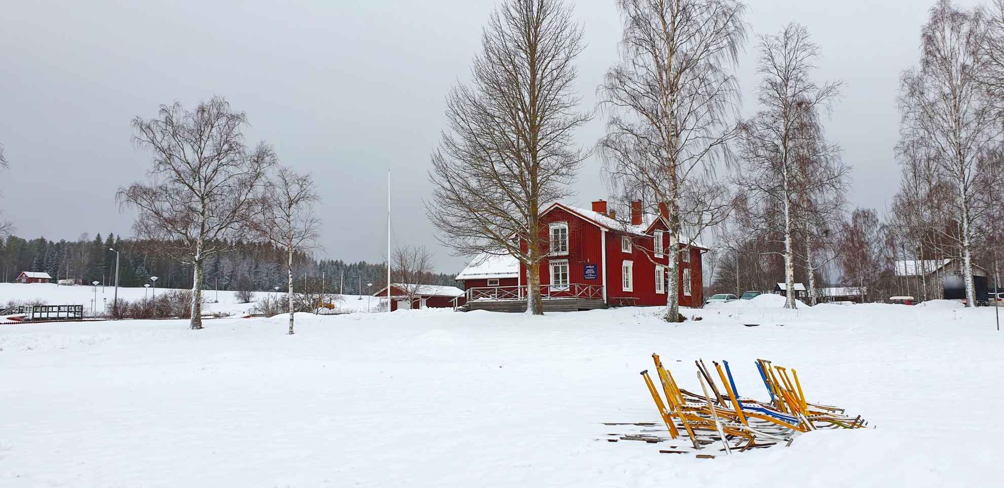 A red house during winter. In front of the house is a set of kick-sleds.