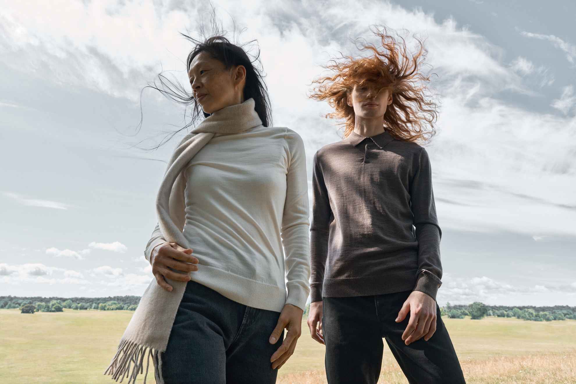 A fashion shoot of two women standing in a field with the wind in their hair.