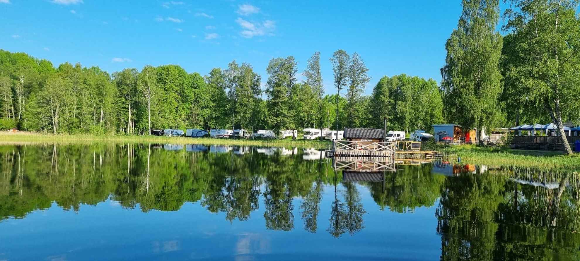 The water in Lake Nossen reflects the surrounding greenery and the mobile homes parked next to the water.