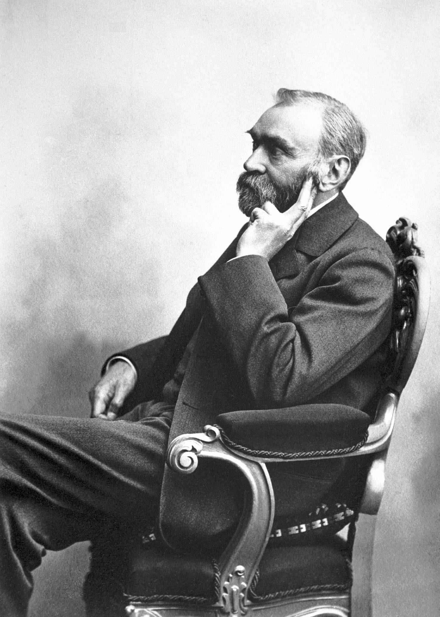 A black and white old portrait of Alfred Nobel sitting in a chair.