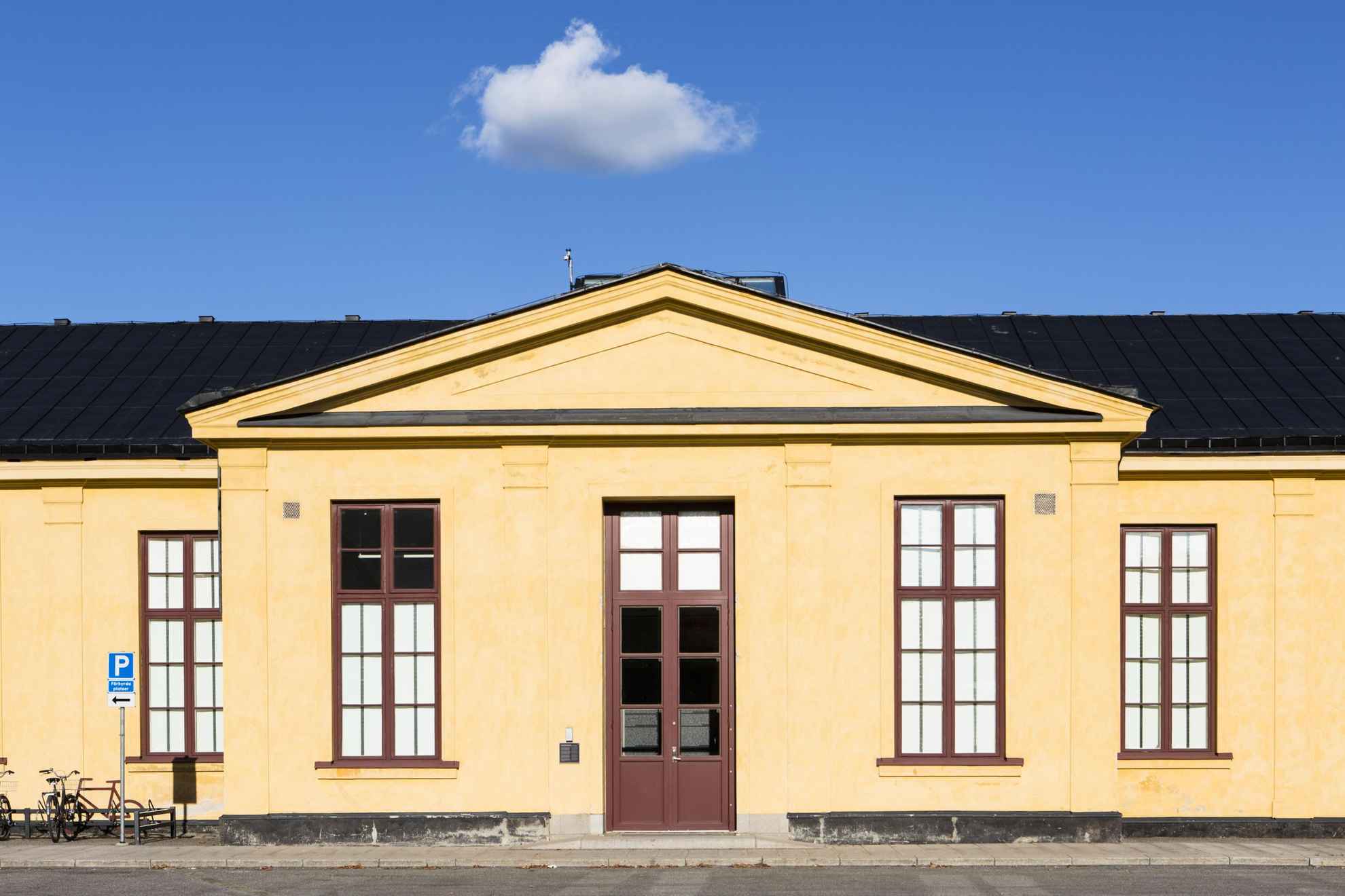 The exterior of a light yellow building with burgundy mullioned windows and a double door.
