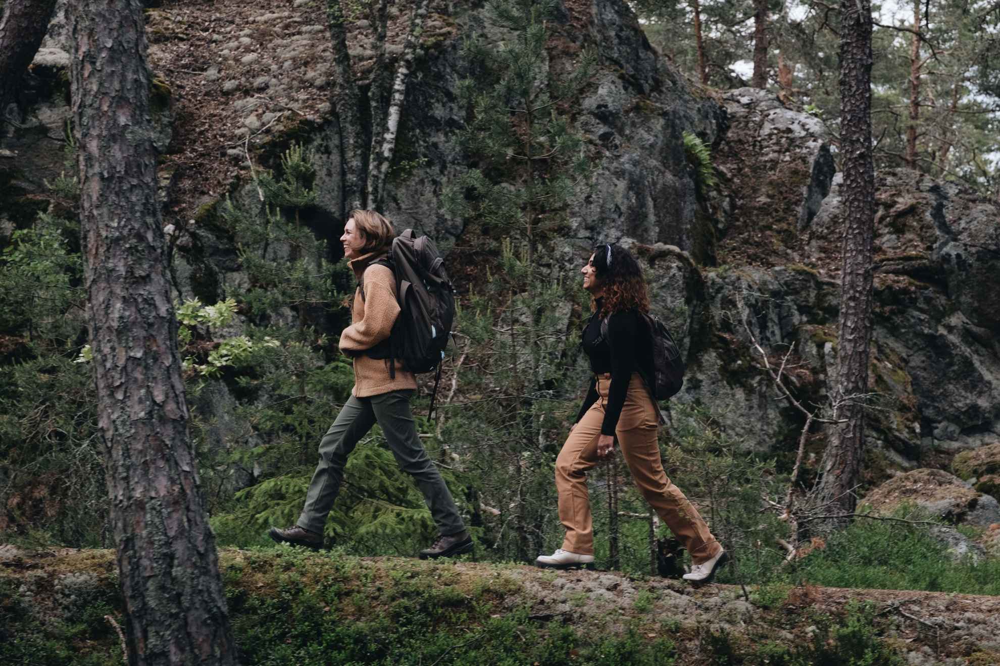 Two women in outdoor clothing hiking in a forest.