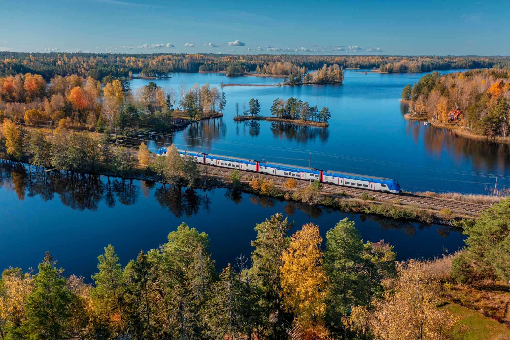 An aerial view of a train passing through a forest landscape with lakes in autumn.