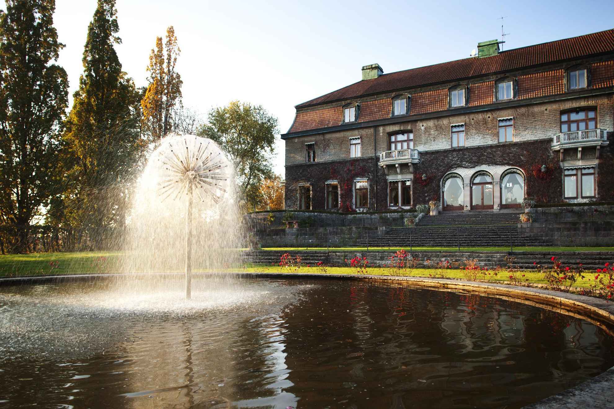A fountain in front of a large building during autumn.