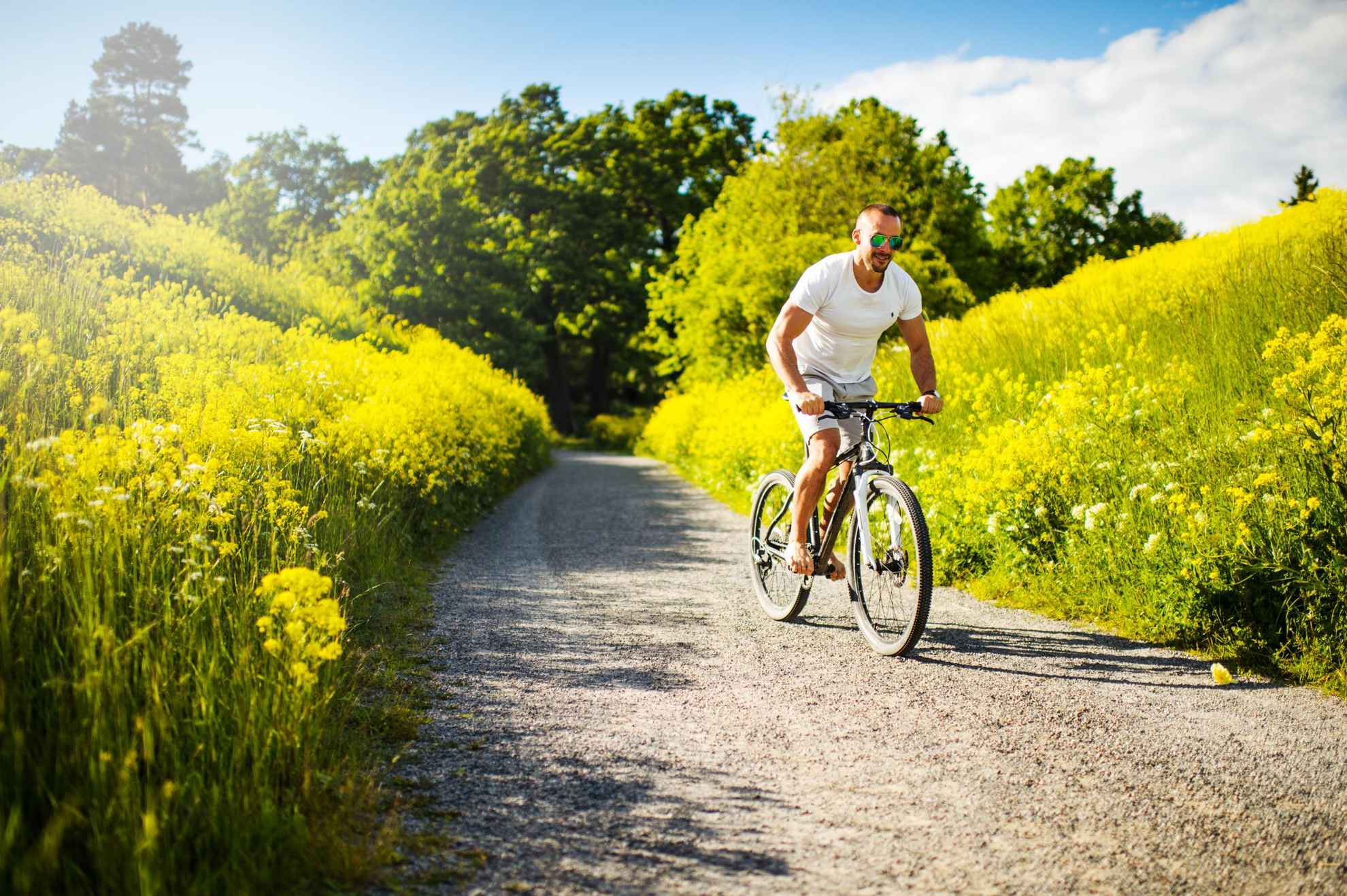 A man rides a bike on a gravel road with fields on both sides of him.
