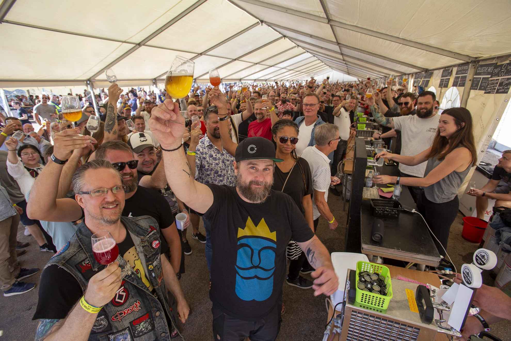 A tent at the Brewskival festival filled with people raising their glasses filled with beer towards the camera.