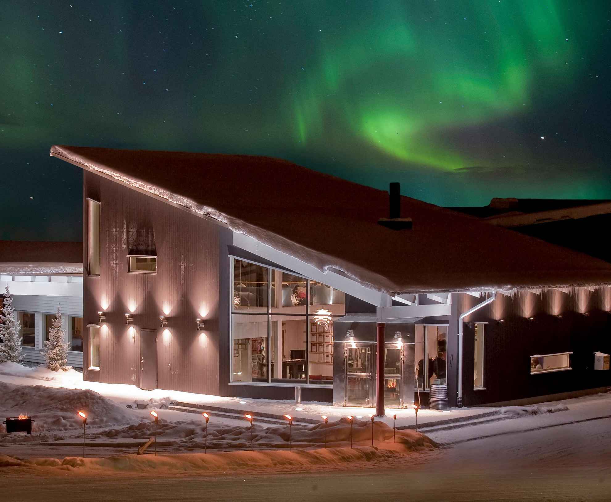 The northern lights is in the sky above a house during night time in winter.