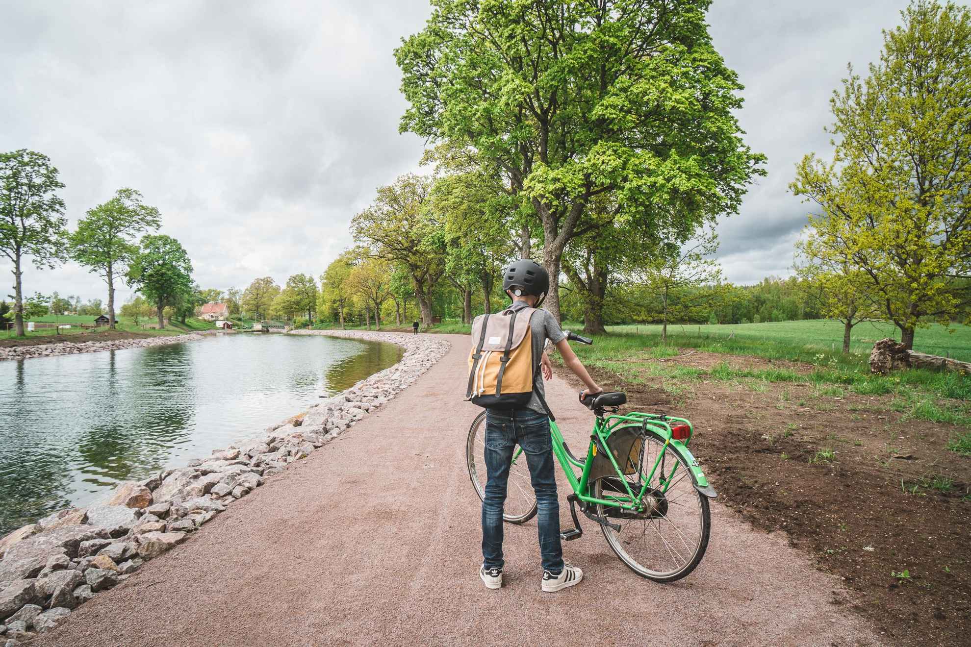 A boy standing next to his green bicycle on a road next to the water of Göta Canal.