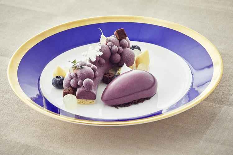 A purple dessert with garnish on a plate in white and blue with a golden edge.