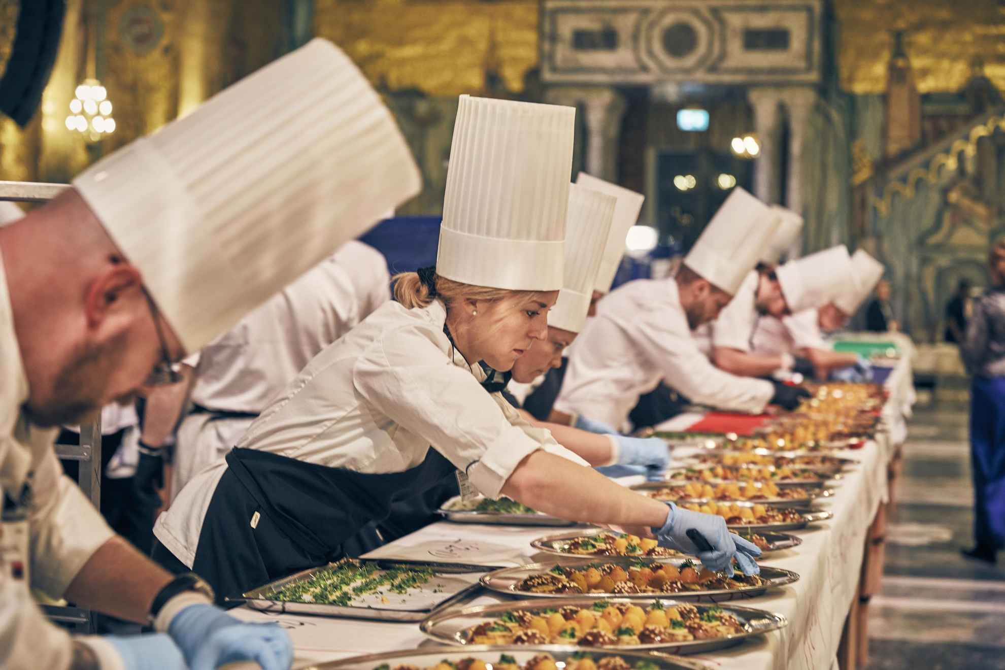 Chefs are standing on a row plating food.
