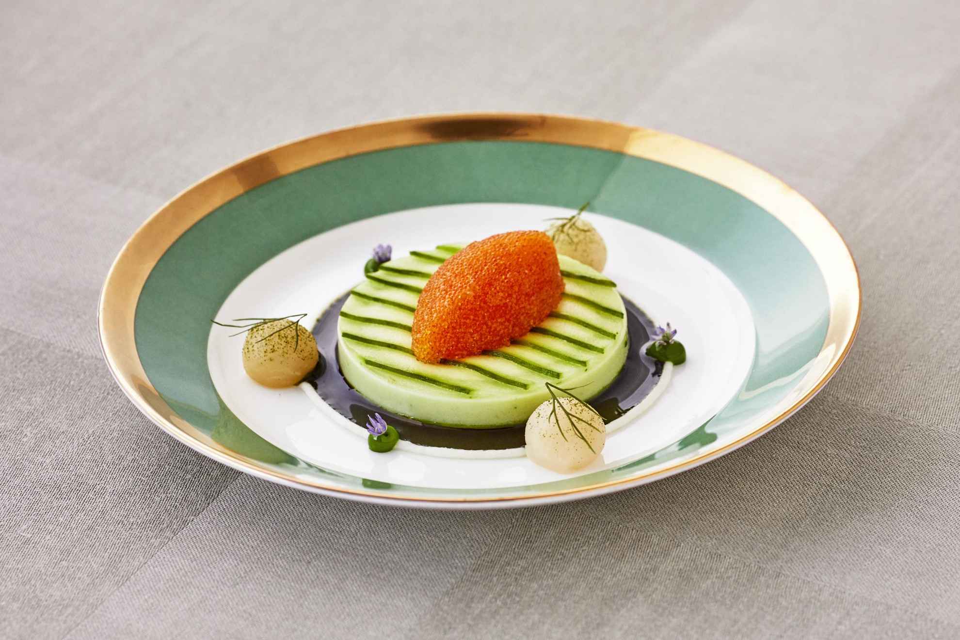 An entrée neatly laid out in a plate in white and green with a golden edge.