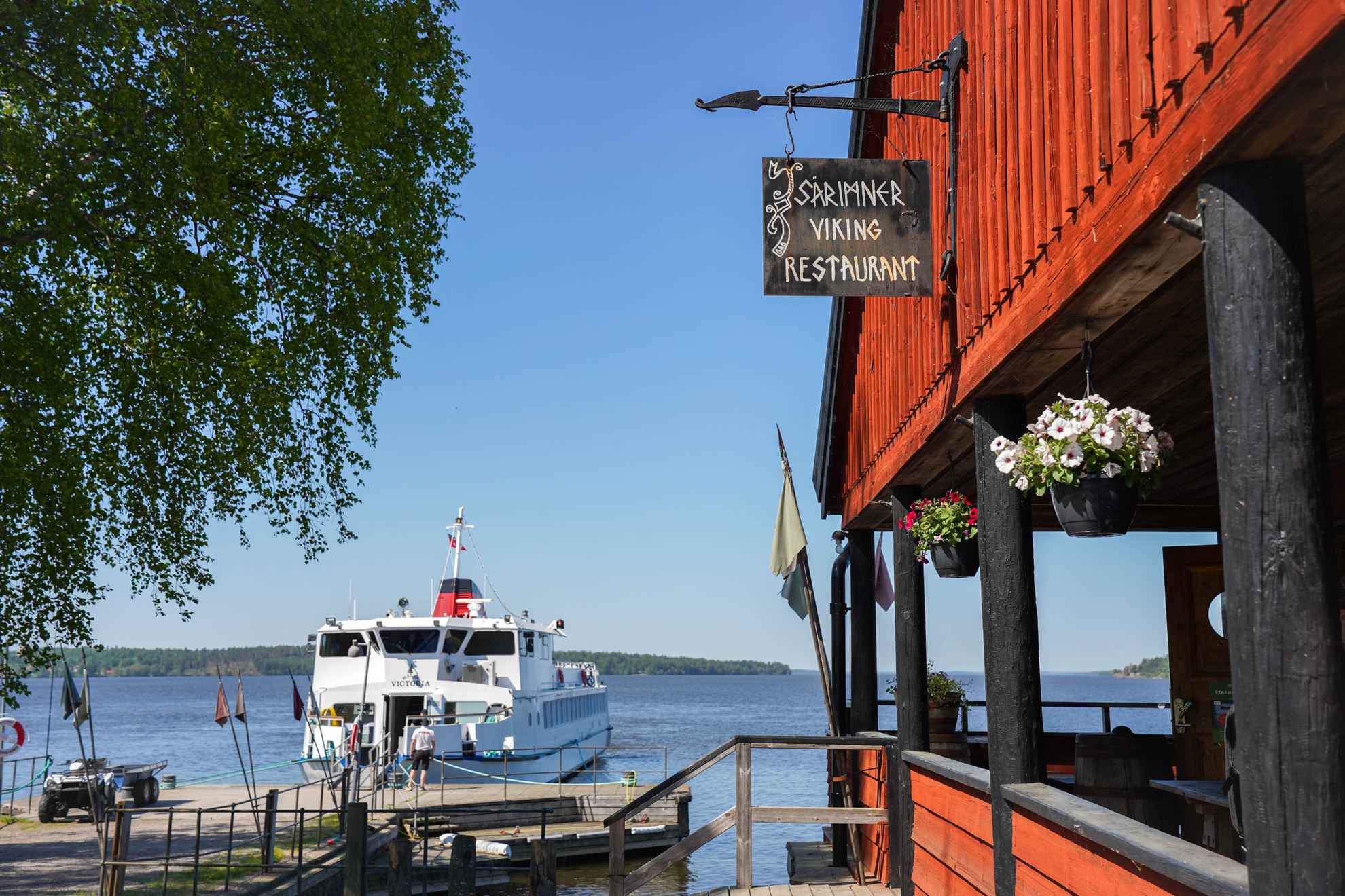 Birka M/S Mälar Victoria arrives by the dock at Birka, Viking Village. Viking restaurant Särimner to the right. Spring time and blue skies in the background.