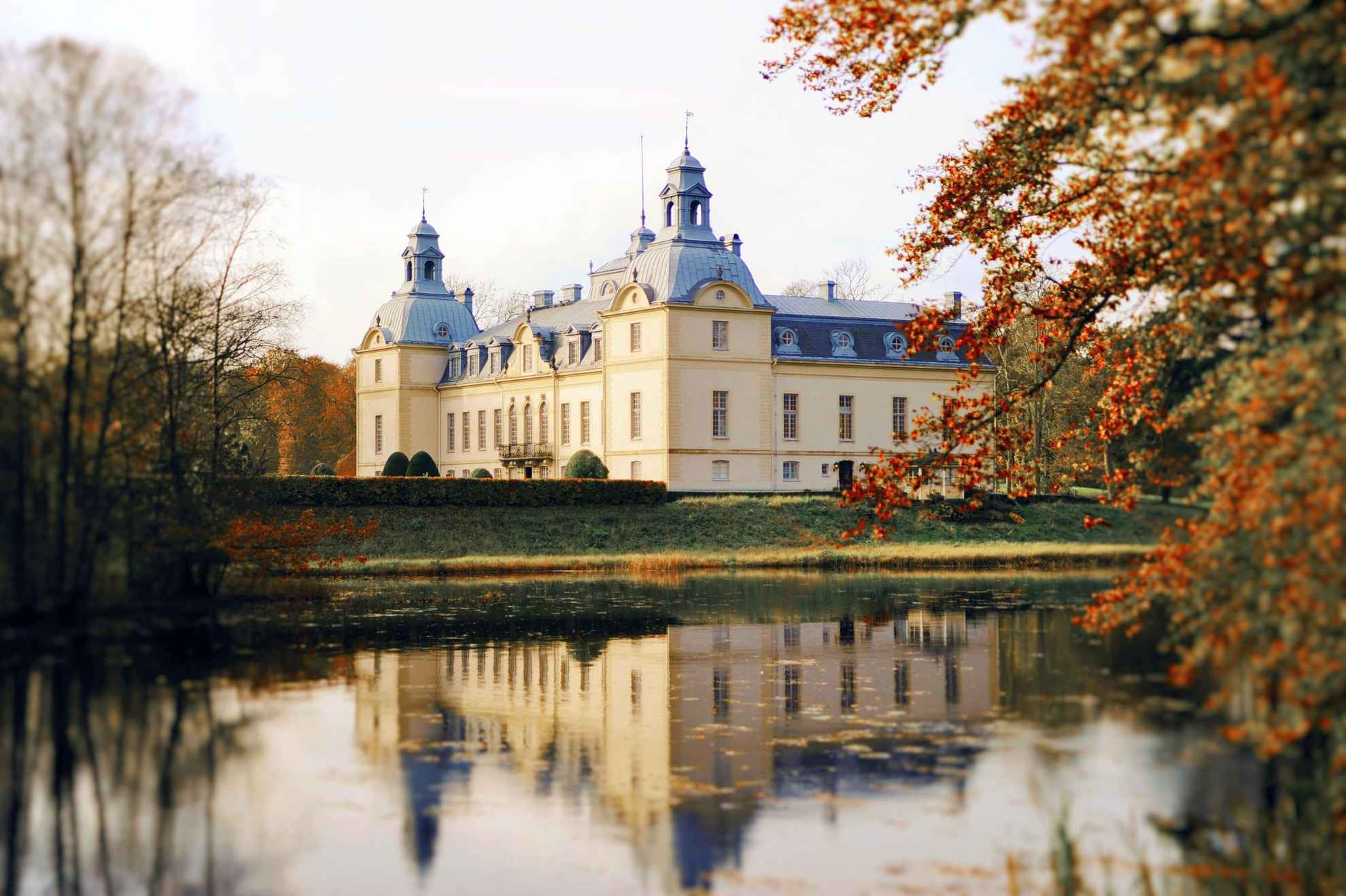 Kronovall Castle next to a lake during autumn. The castle is reflected in the water.