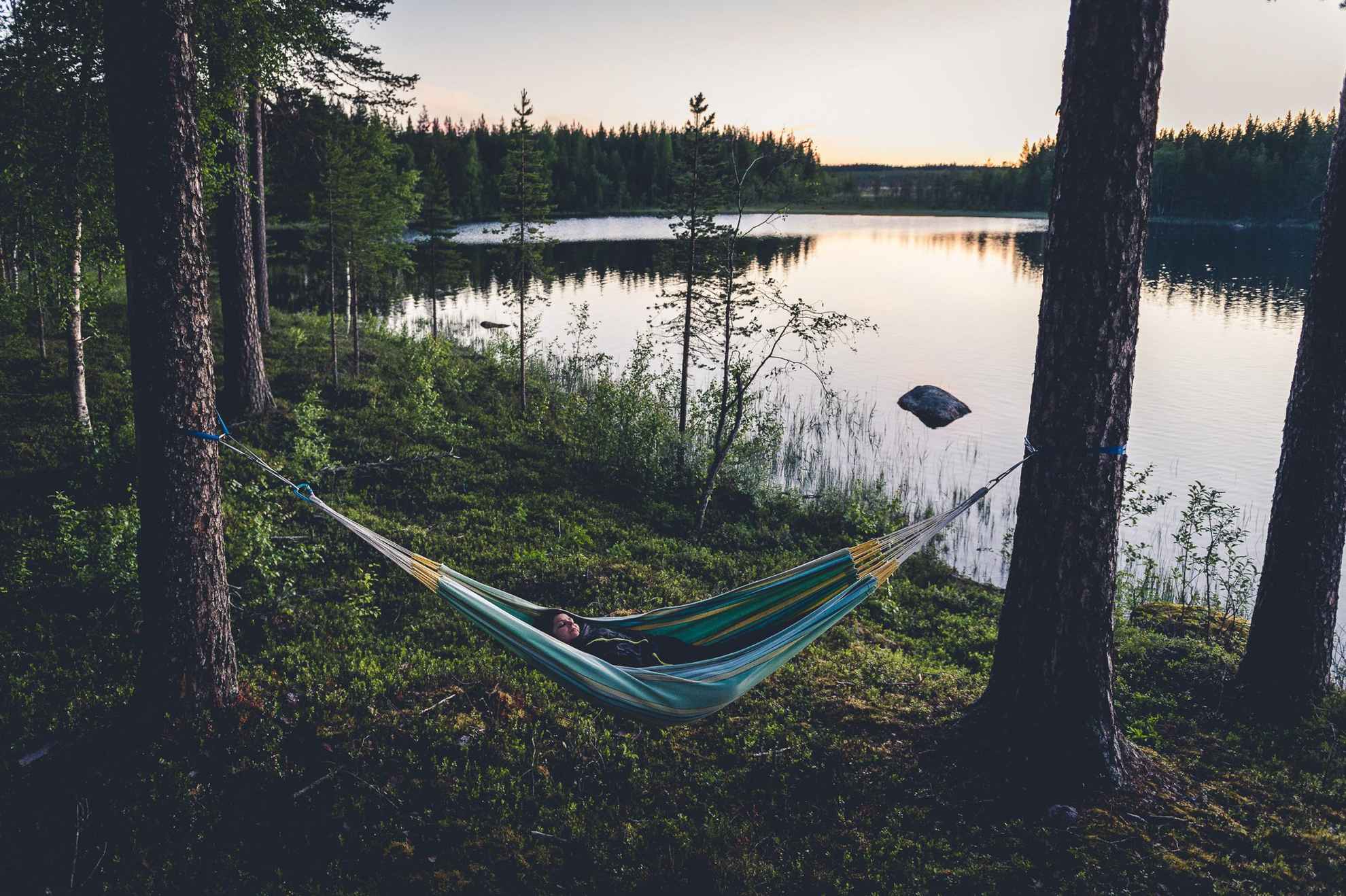 A woman is lying in a hammock in a forest next to a lake.