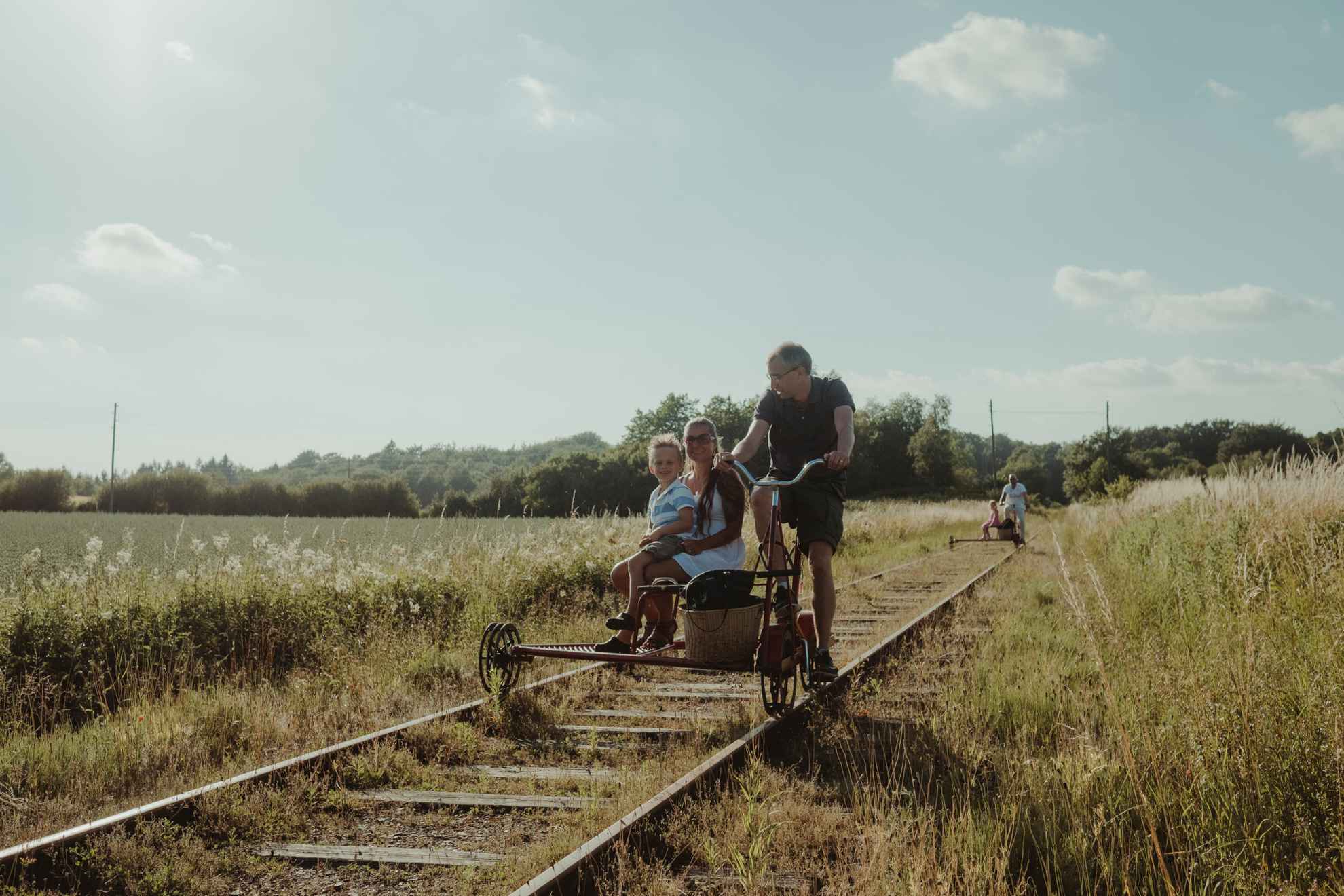 A family on a trolley bike on an old railway, surrounded by fields.