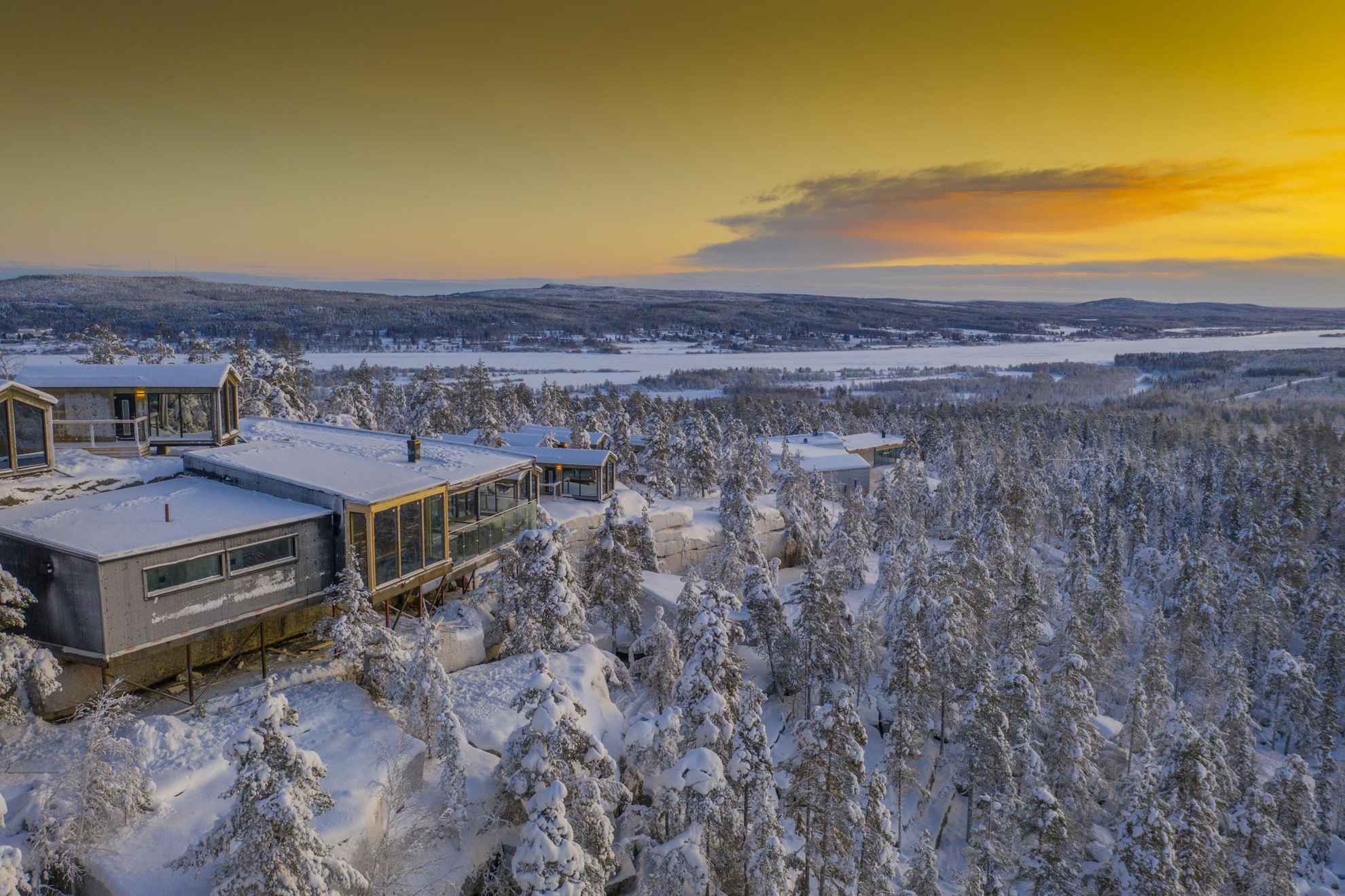 Aerial view of a snow-covered forest and the chalets at Lapland View Lodge during sunset.