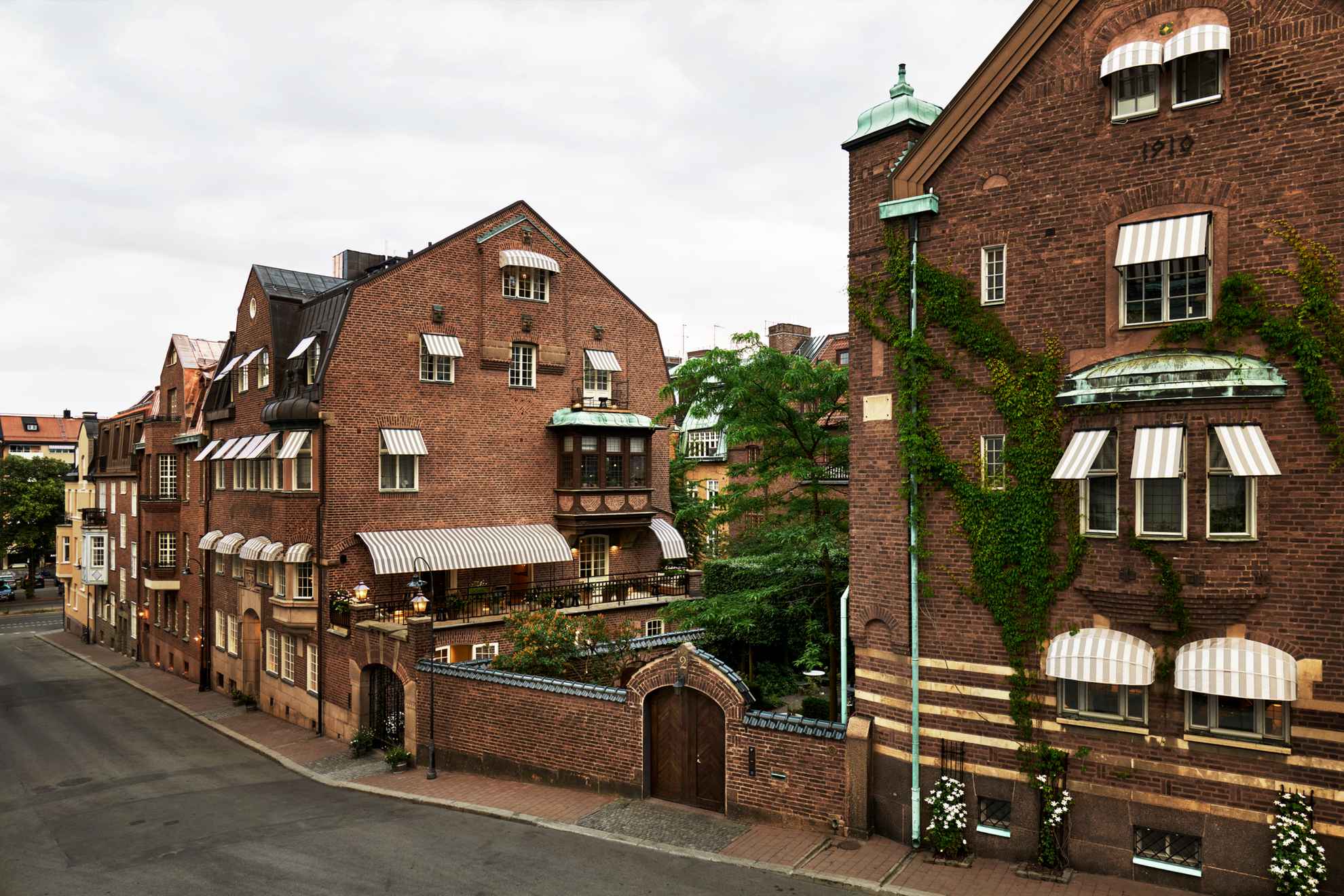 Exterior of an old four story brick house with a garden where you see the top of a flowering bush.