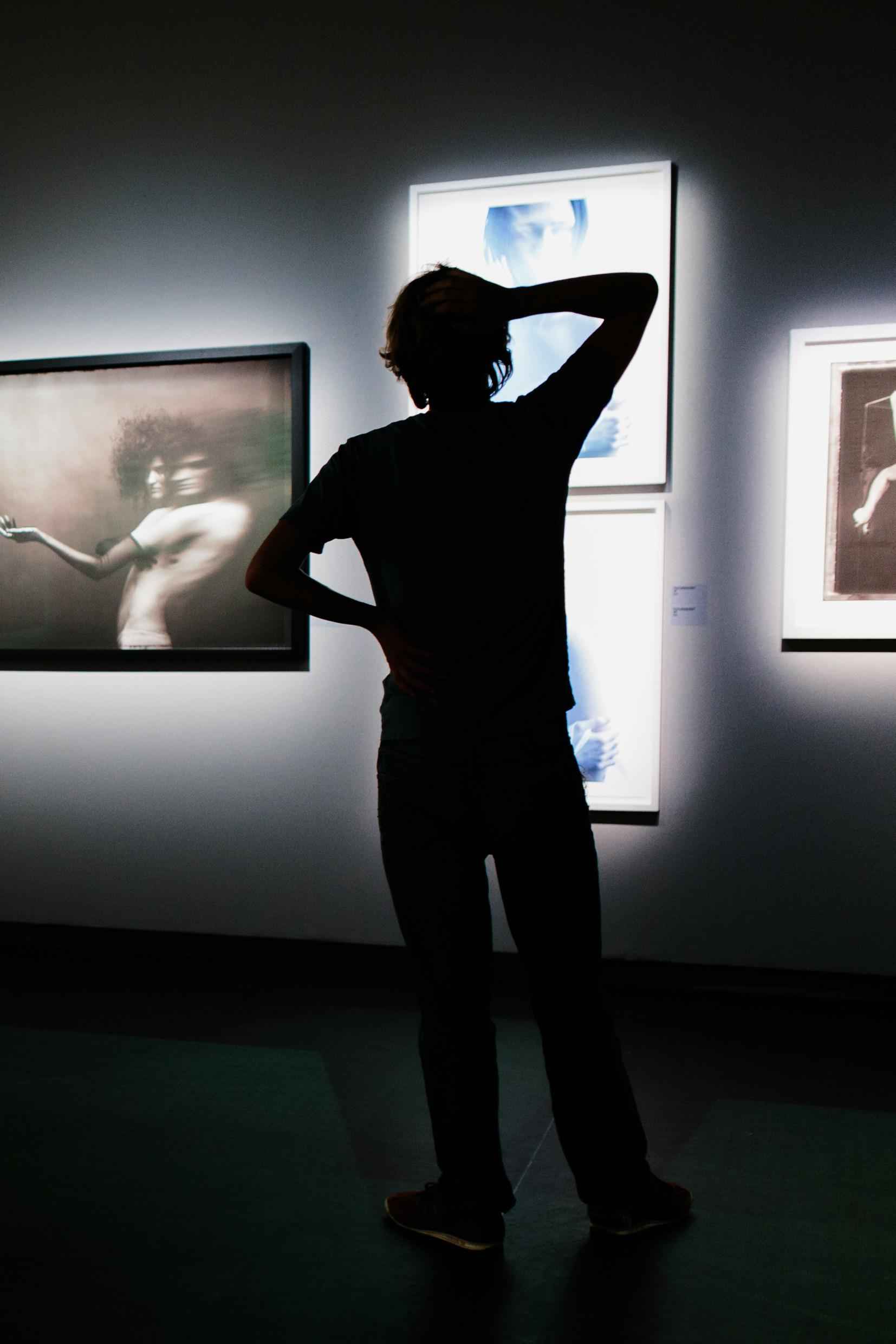 A silhouette of a person looking at photographs in an exhibition.
