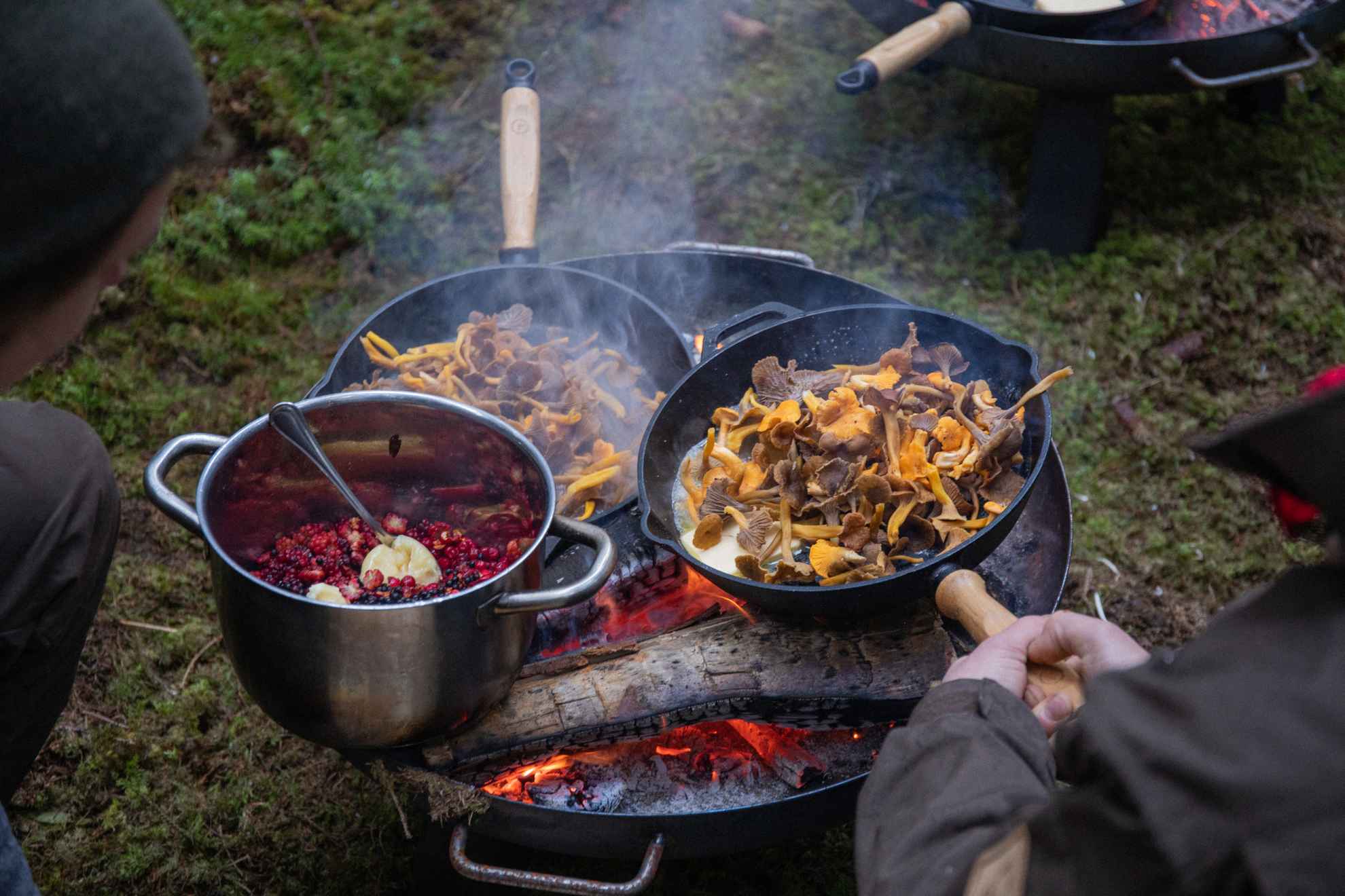 People frying chanterelle and boiling berries outdoors.