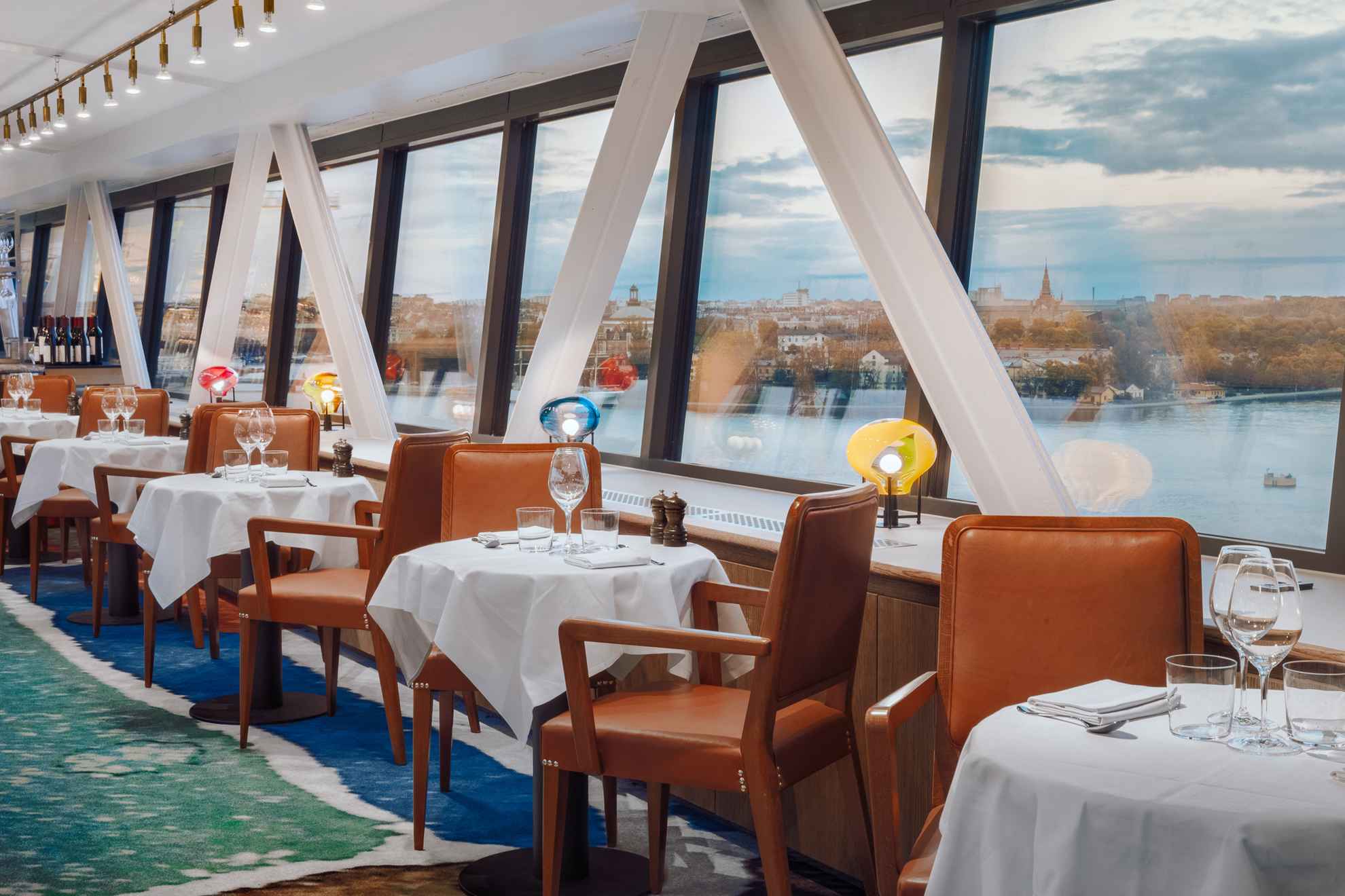 Tables and chairs at restaurant Gondolen with large windows overlooking the water.