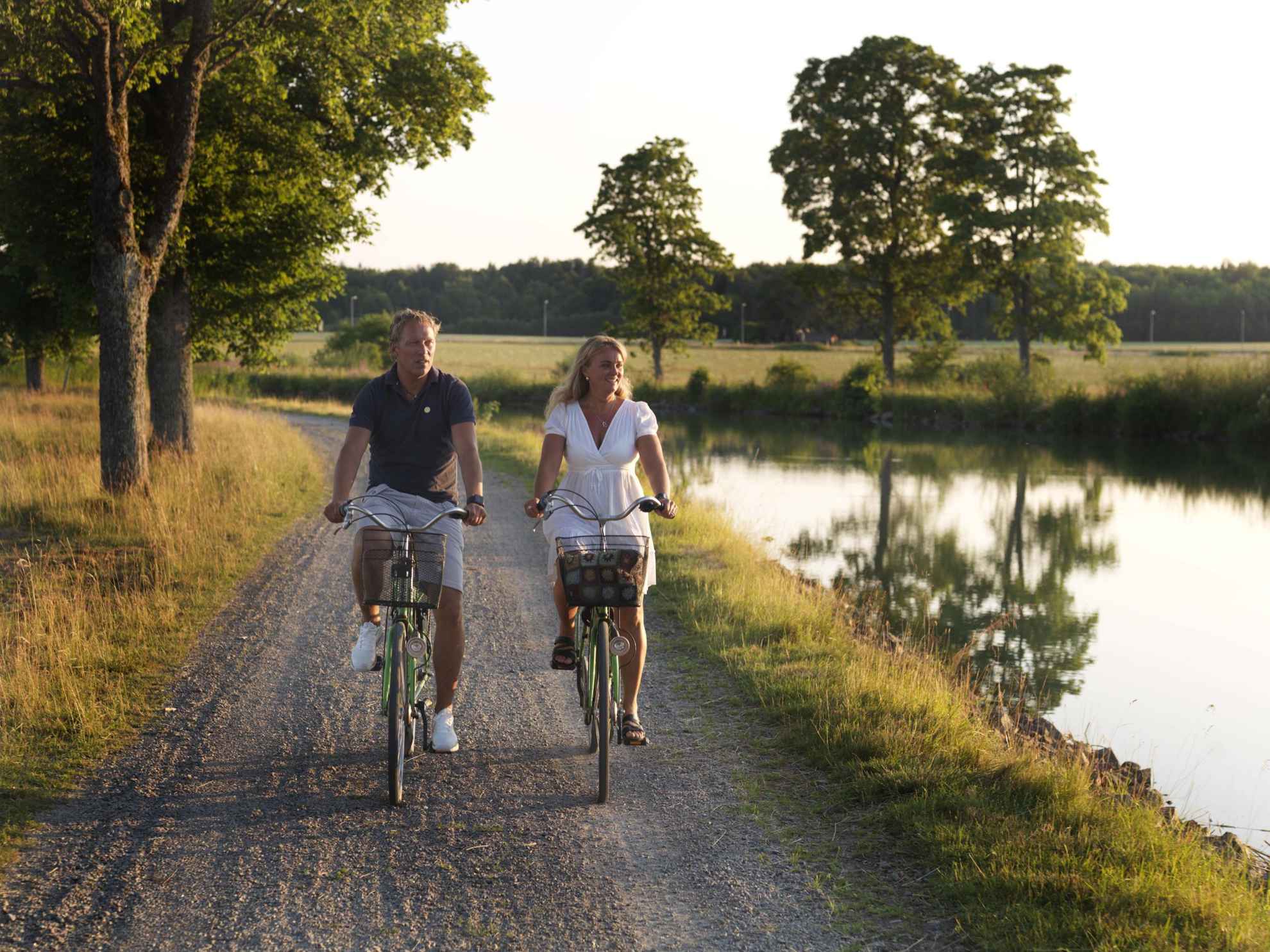 A man and a women biking next to Göta Canal during summer.