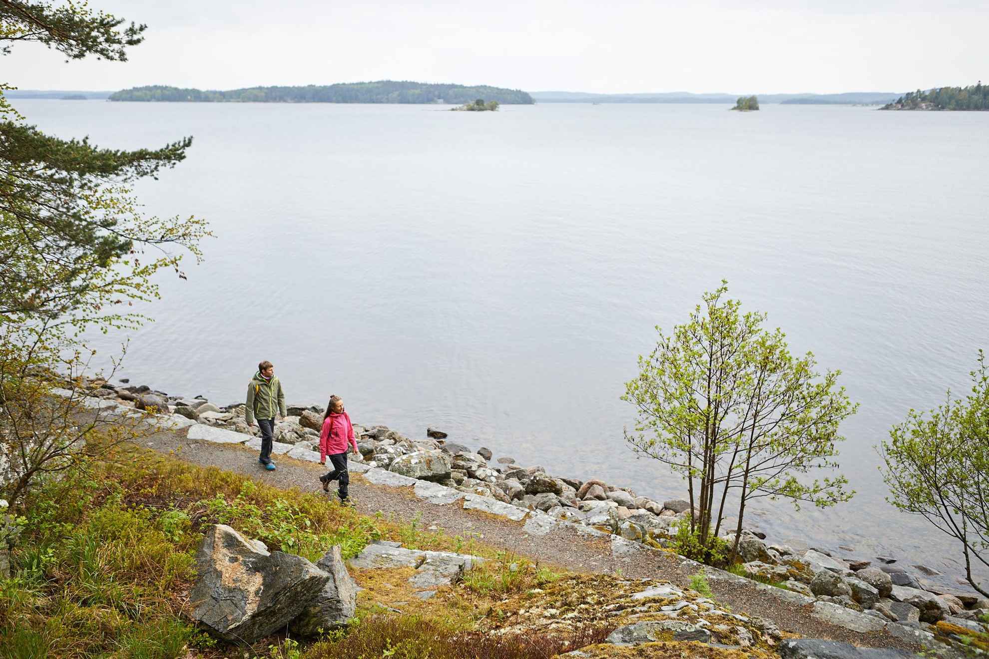 Two persons are walking along the shore with a view of a lake with in West Sweden. You see some islands in the lake.