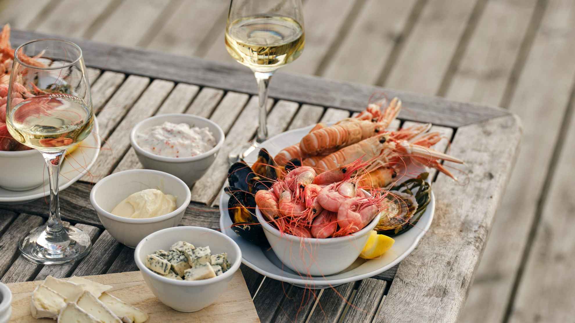 A seafood platter and a glass of white wine on a table set on a jetty.