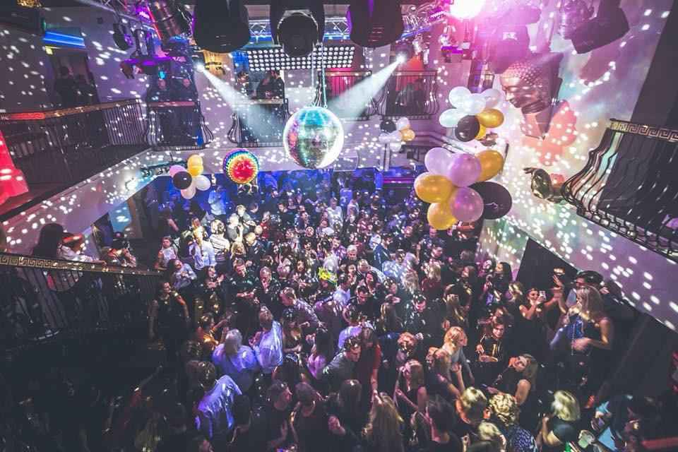 People dancing at a nightclub. There are balloons and decoration hanging from the ceiling.