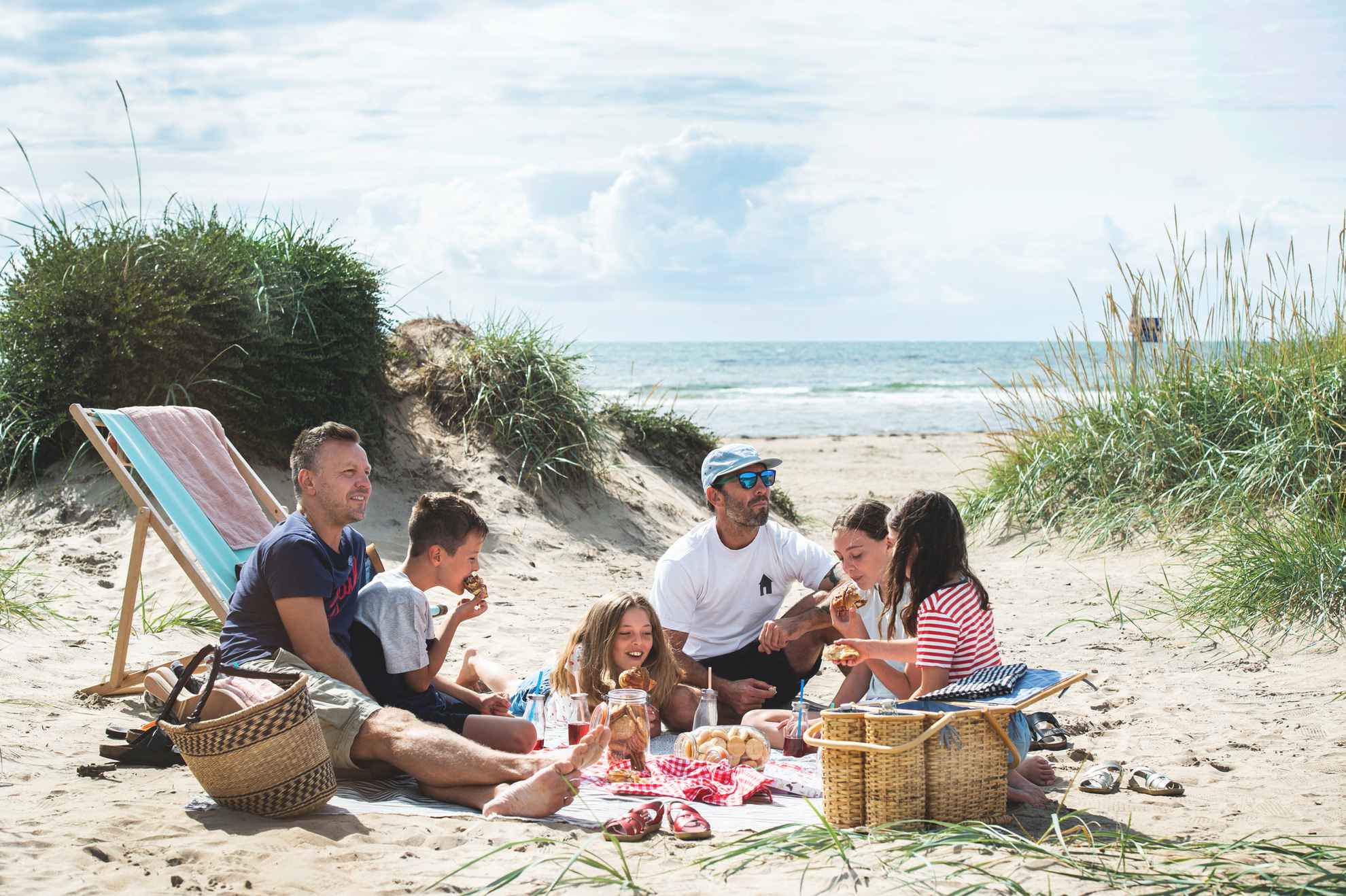 Two men and four children having picnic on the beach.