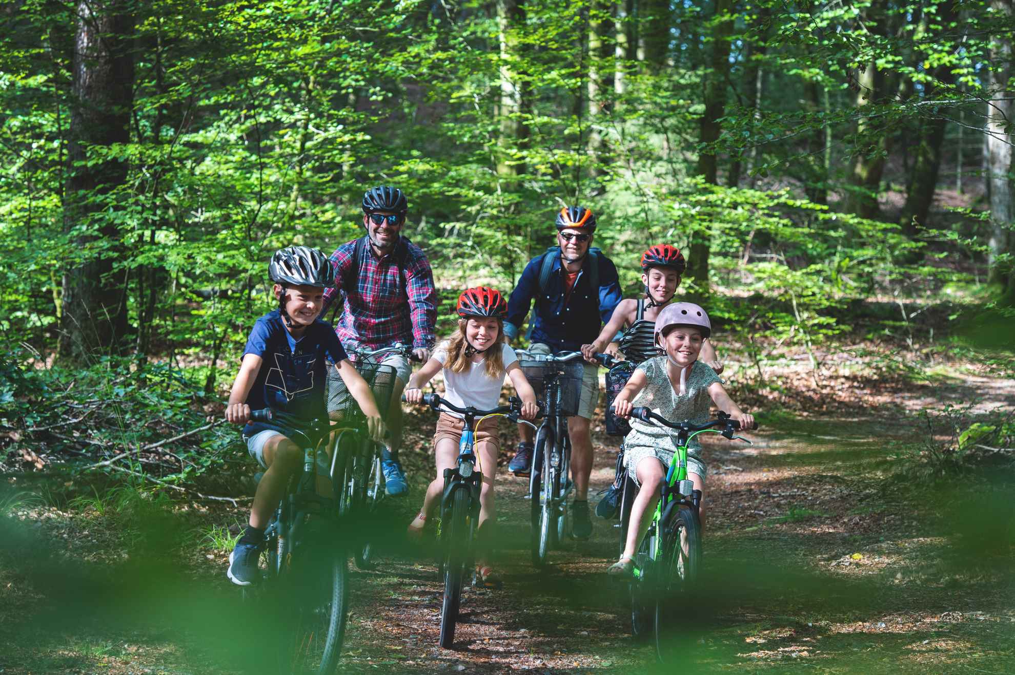 Two men and four children biking in the forest.