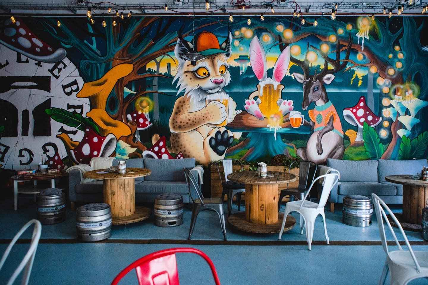 Wooden table with beer barrels as chairs, with a colourful graphite wall behind.