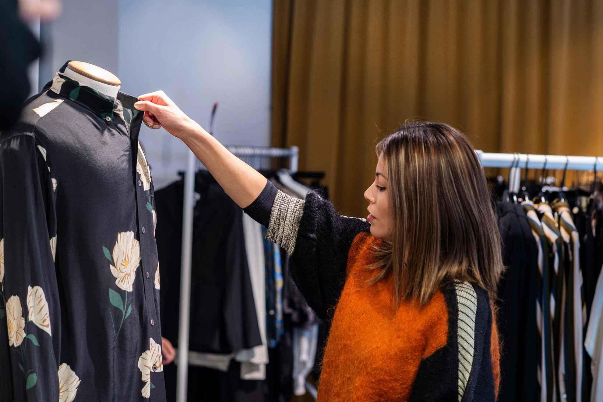 A woman touching and looking at a shirt with a floral pattern on a mannequin in a shop.