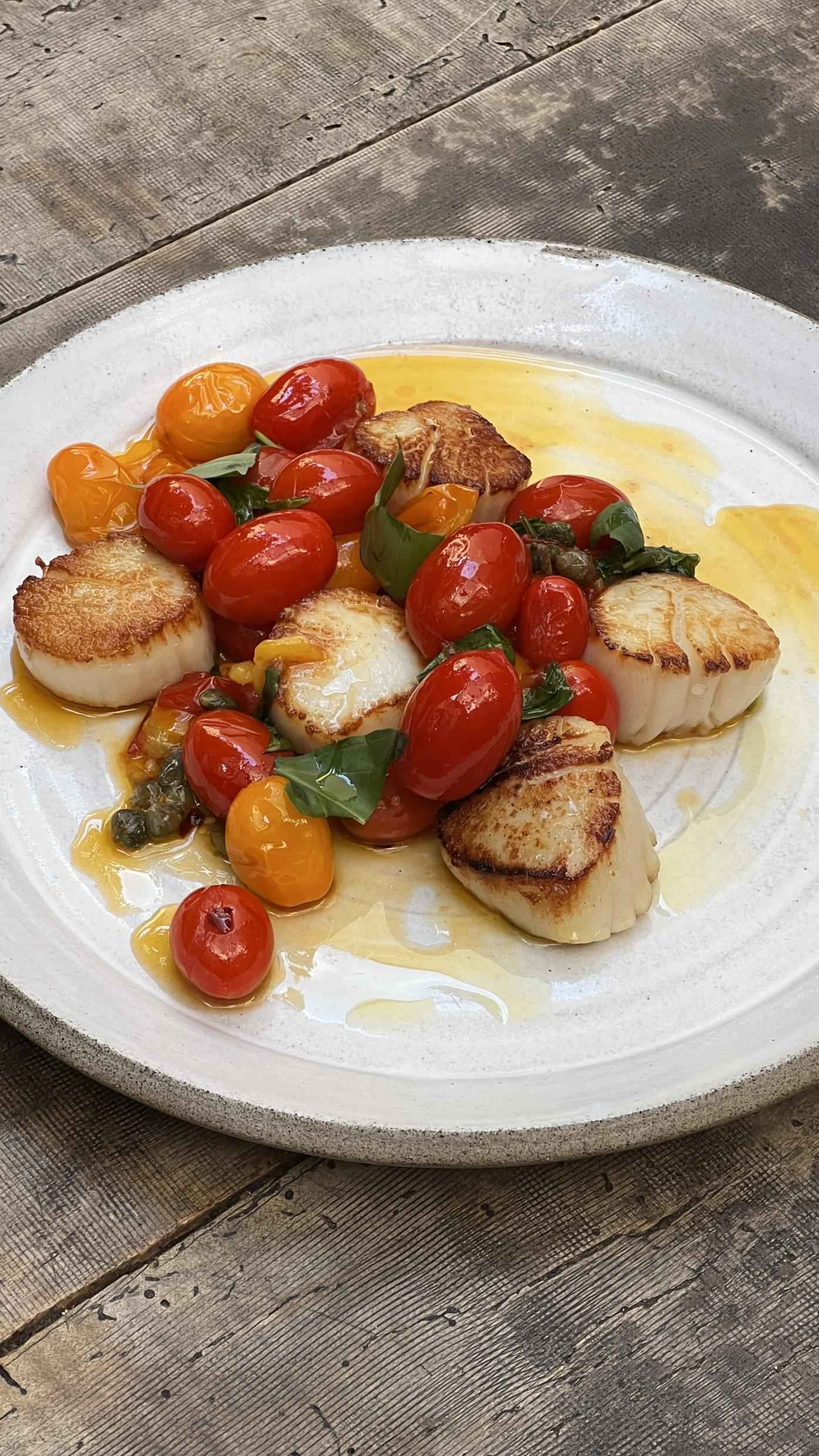 A plate with scallops, tomatoes, basil and vinaigrette.