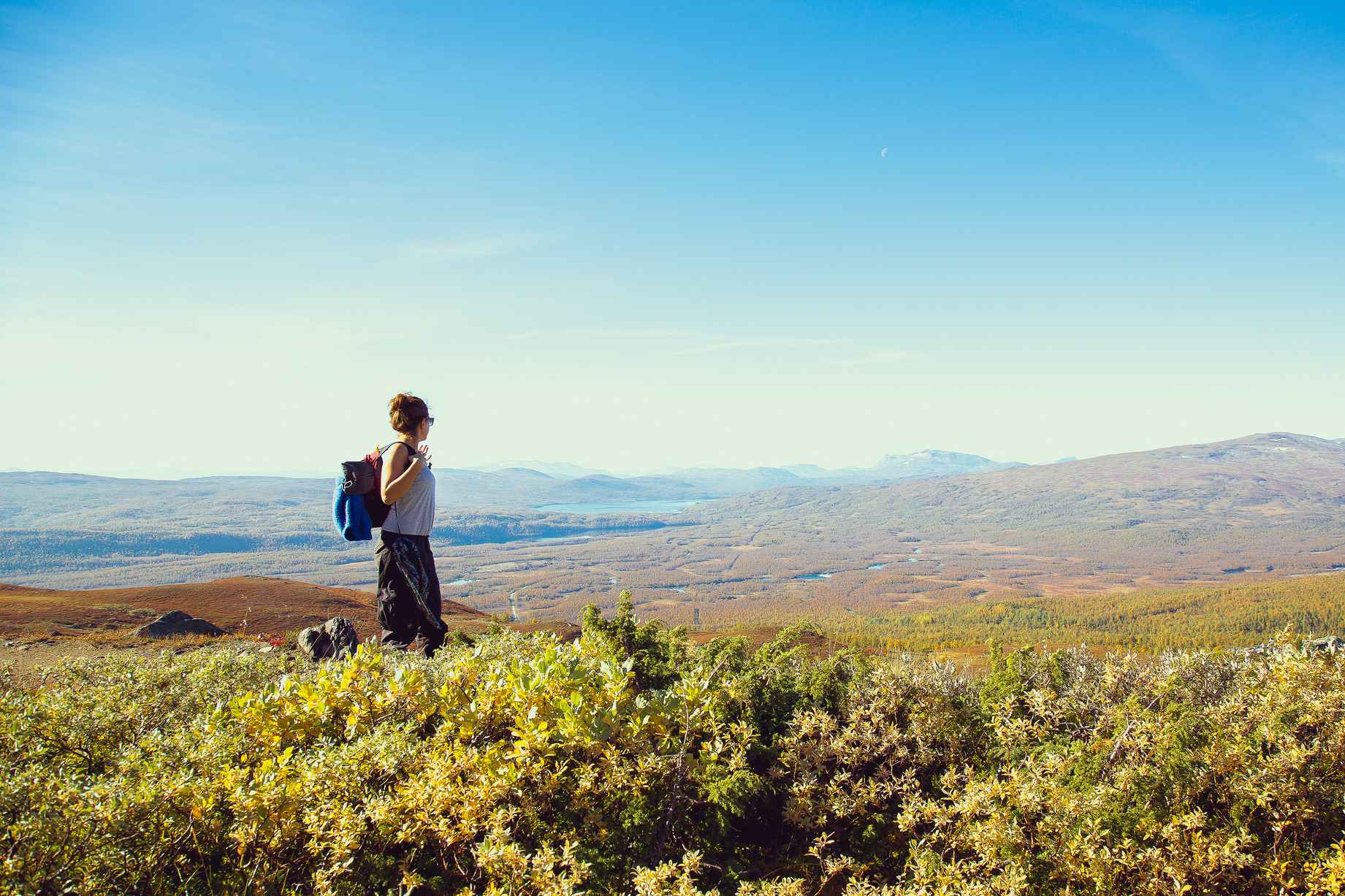 Woman hiking with a backpack, gazing out over mountainous terrain on a sunny day.
