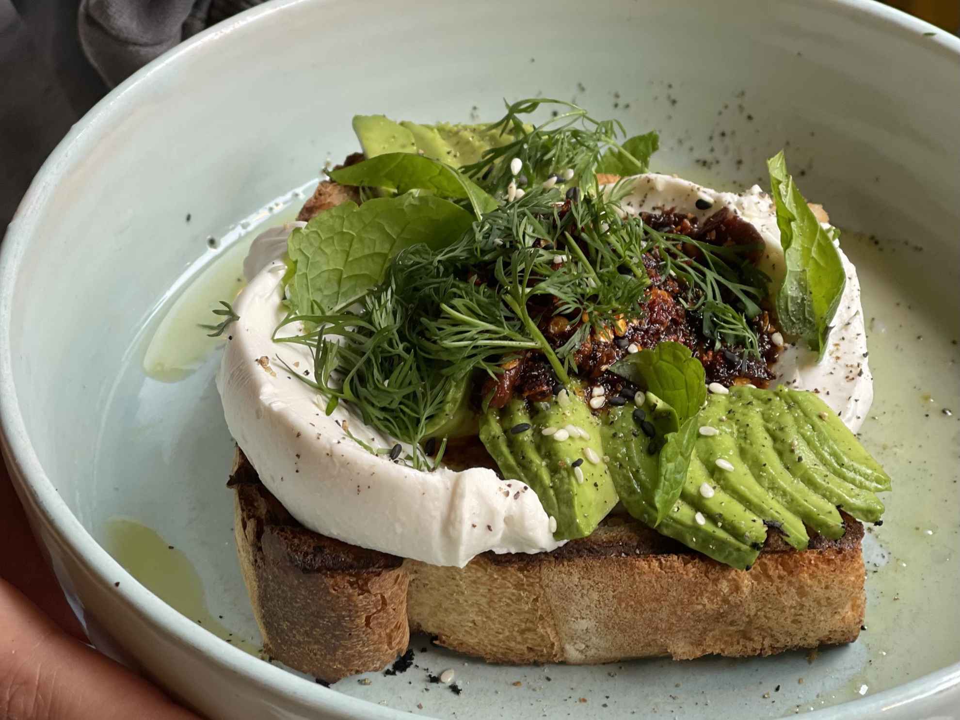 A plate with a sandwich with avocado and other ingredients.