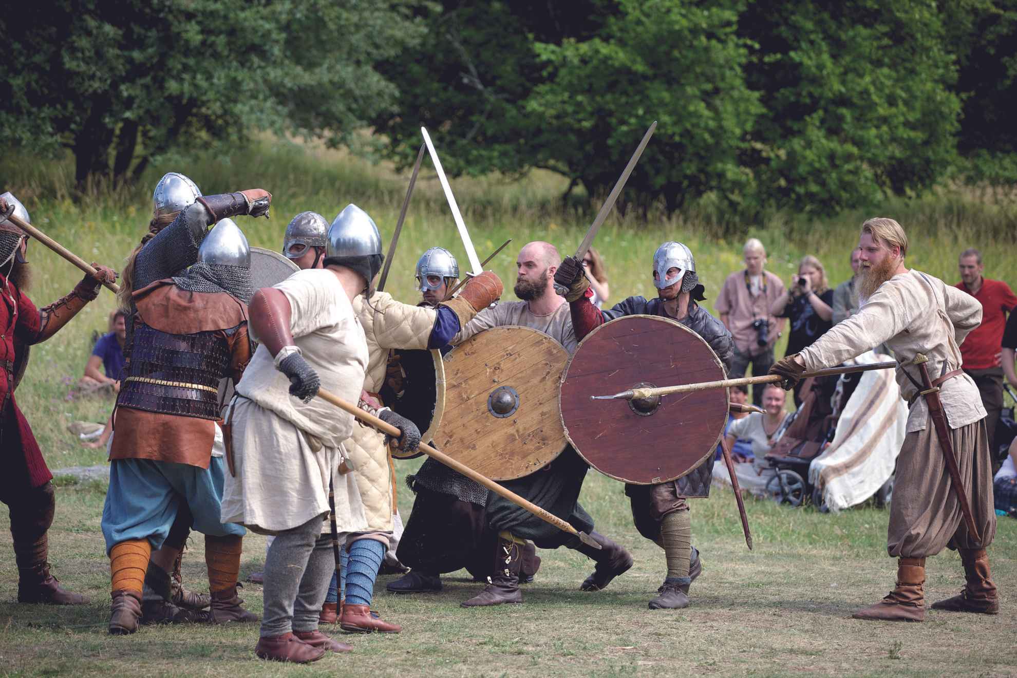 A group of people, all dressed up in viking clothing, is reenacting a battle with spears, swords and shields.