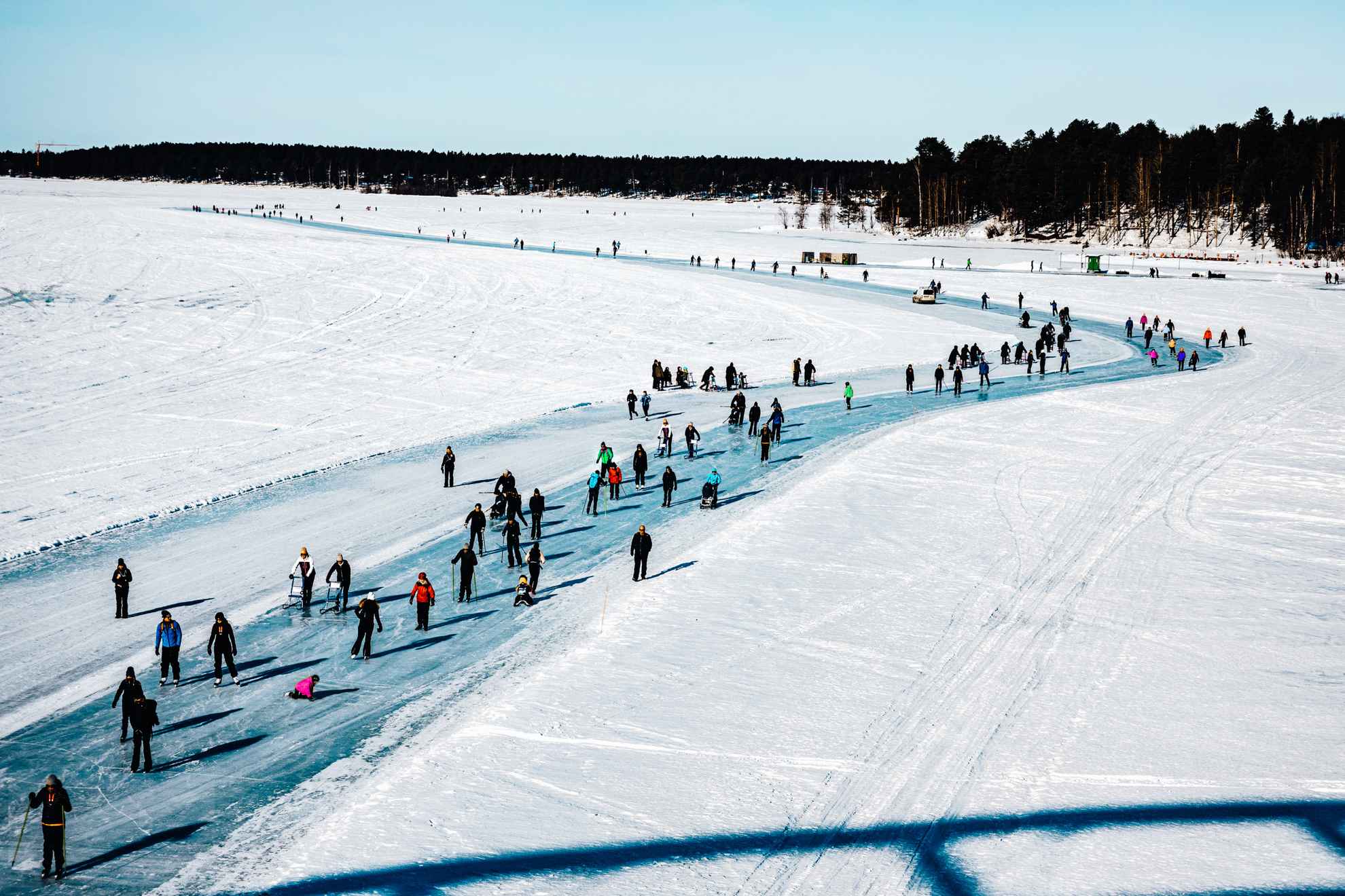People walking and skating on the sunny ice track encircling Luleå