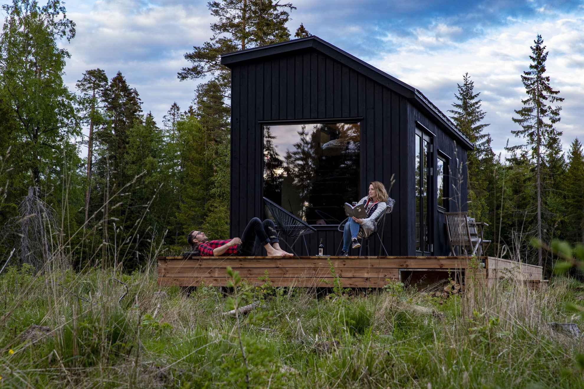 Two people are enjoying the sun while sitting on a patio in front of a cabin during summer.