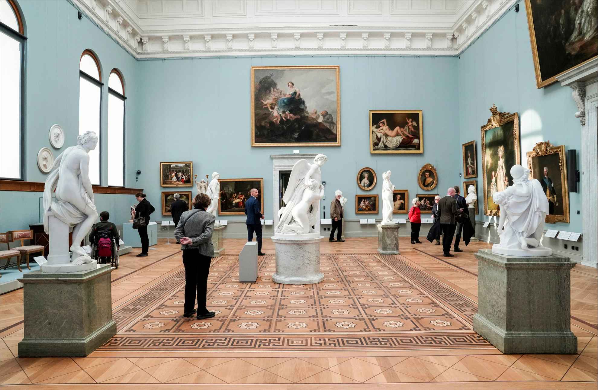 People are walking around in a large room with paintings and sculptures.