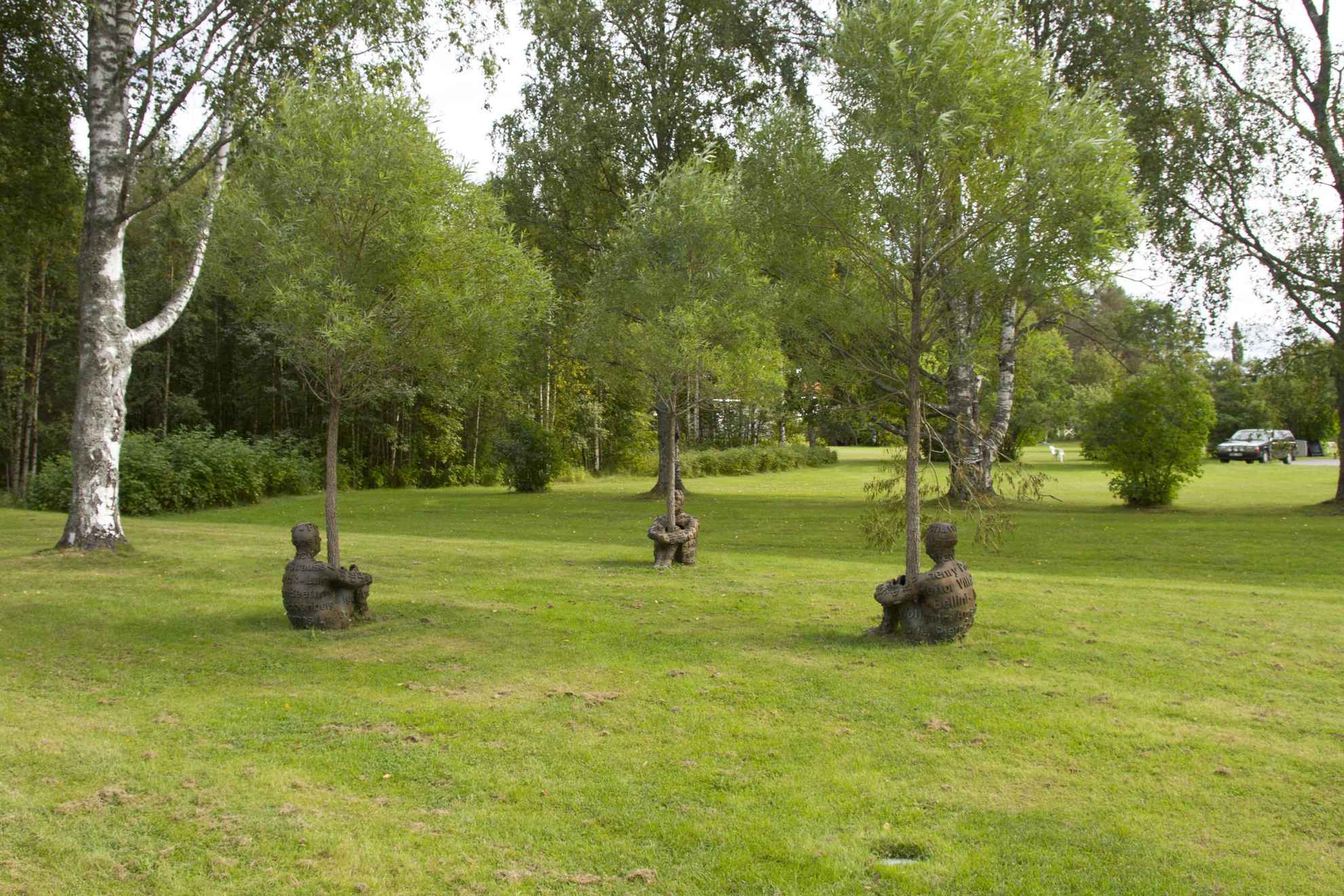 Sculptures named “Heart of Trees”, three people in bronze with their arms and legs wrapped around a tree trunk, in a sculpture park.