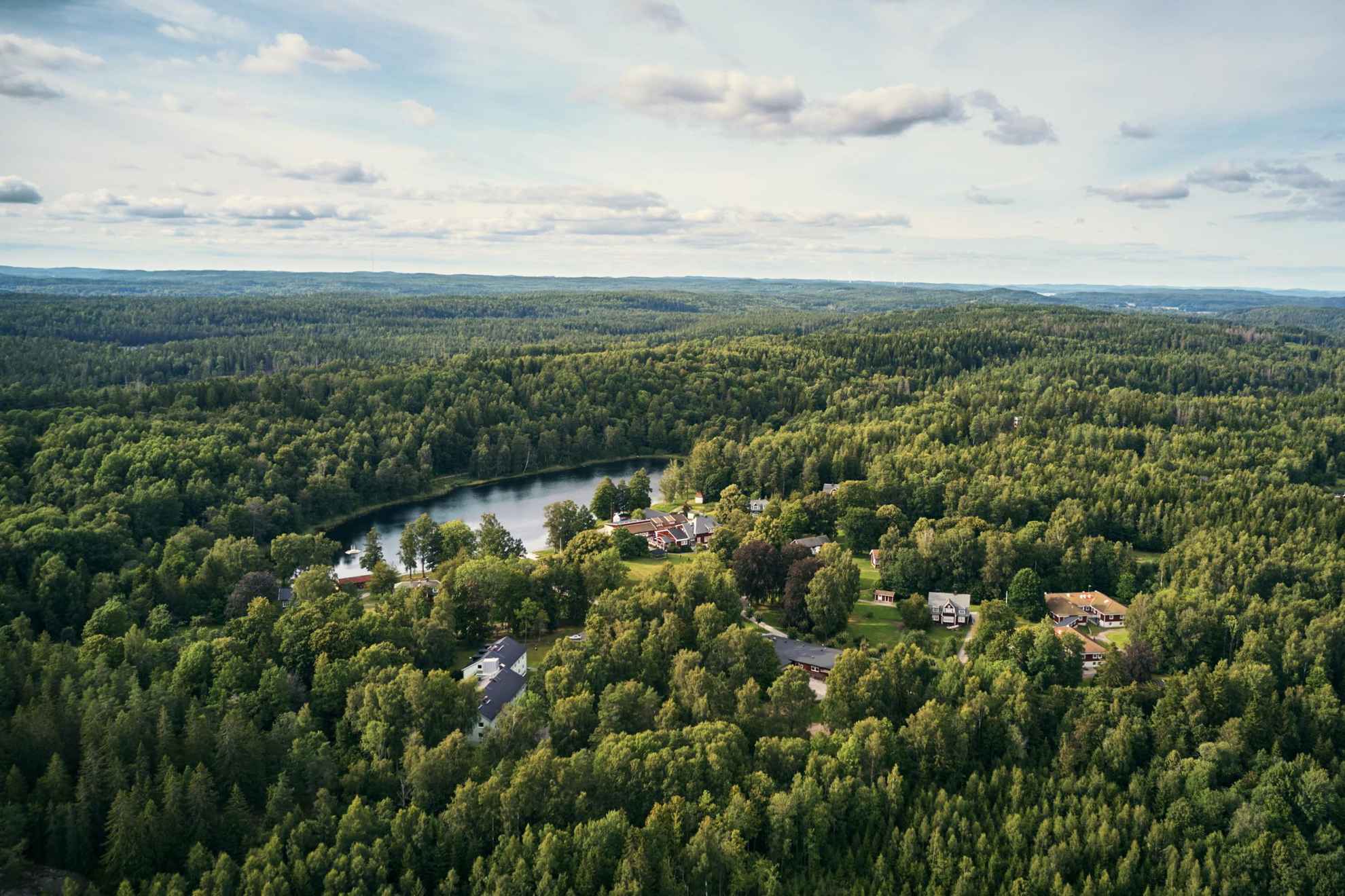 An aerial view of the Kroppefjäll forest during summer. A couple of houses are visible between the trees.
