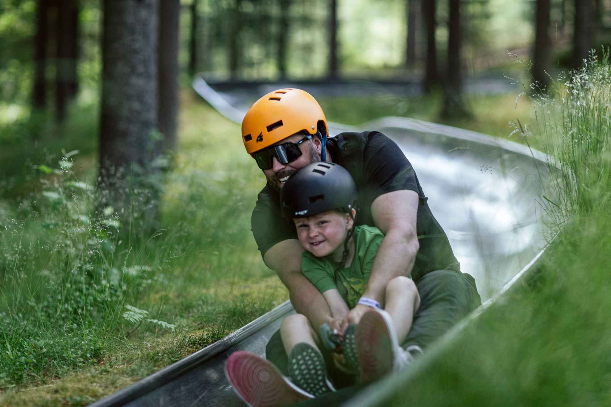 Smiling man and young boy enjoying summer tobogganing at Kungsbygget Adventure Park in Halland.