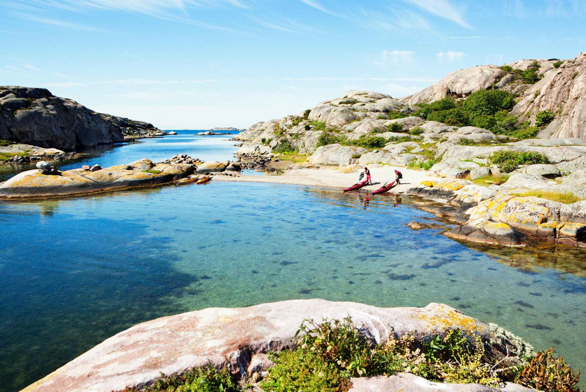 Two people standing next to their kayaks on a beach in the archipelago during a sunny day.