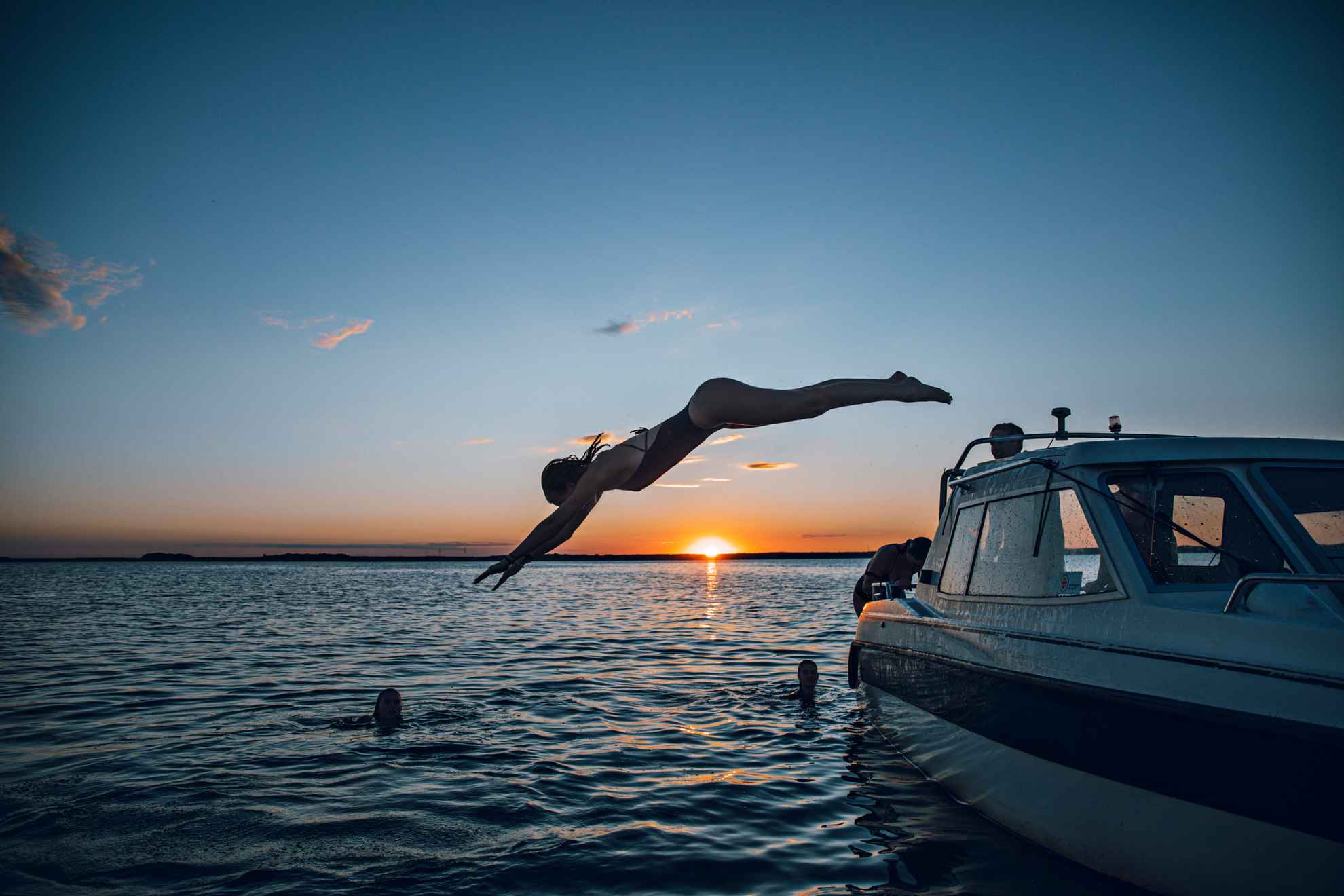 A woman is jumping from a boat in the swedish summer, and the sun is to set