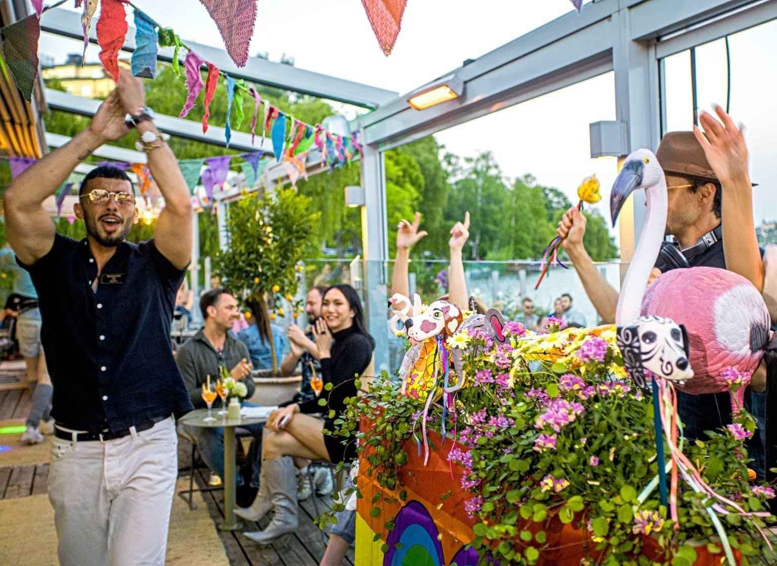 People enjoying a festive moment at Mälarpaviljongen, with a colorful setting and a pink flamingo in the foreground