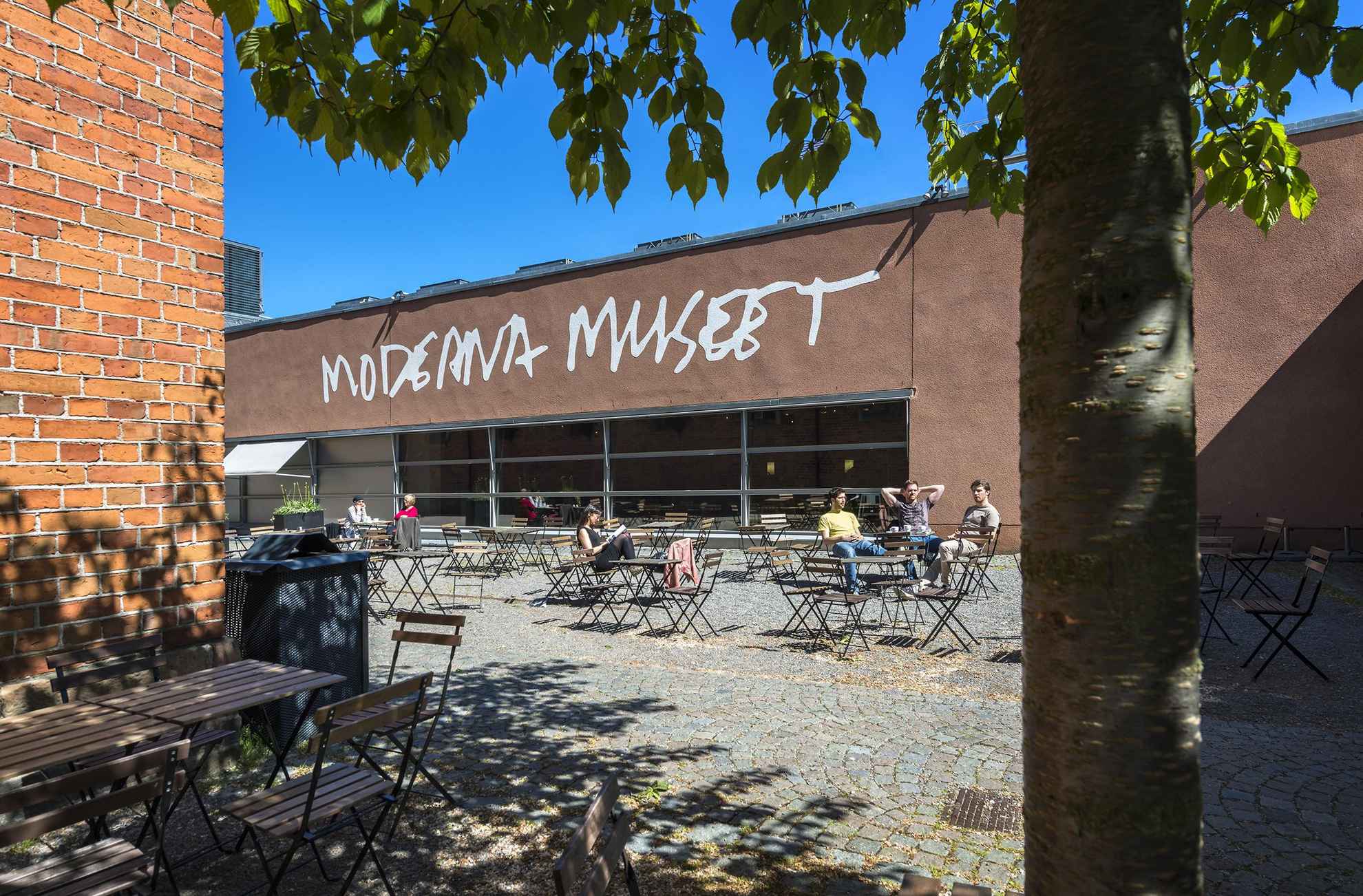 The enterence to Moderna Museet on a sunny day with people sitting on chairs outside.